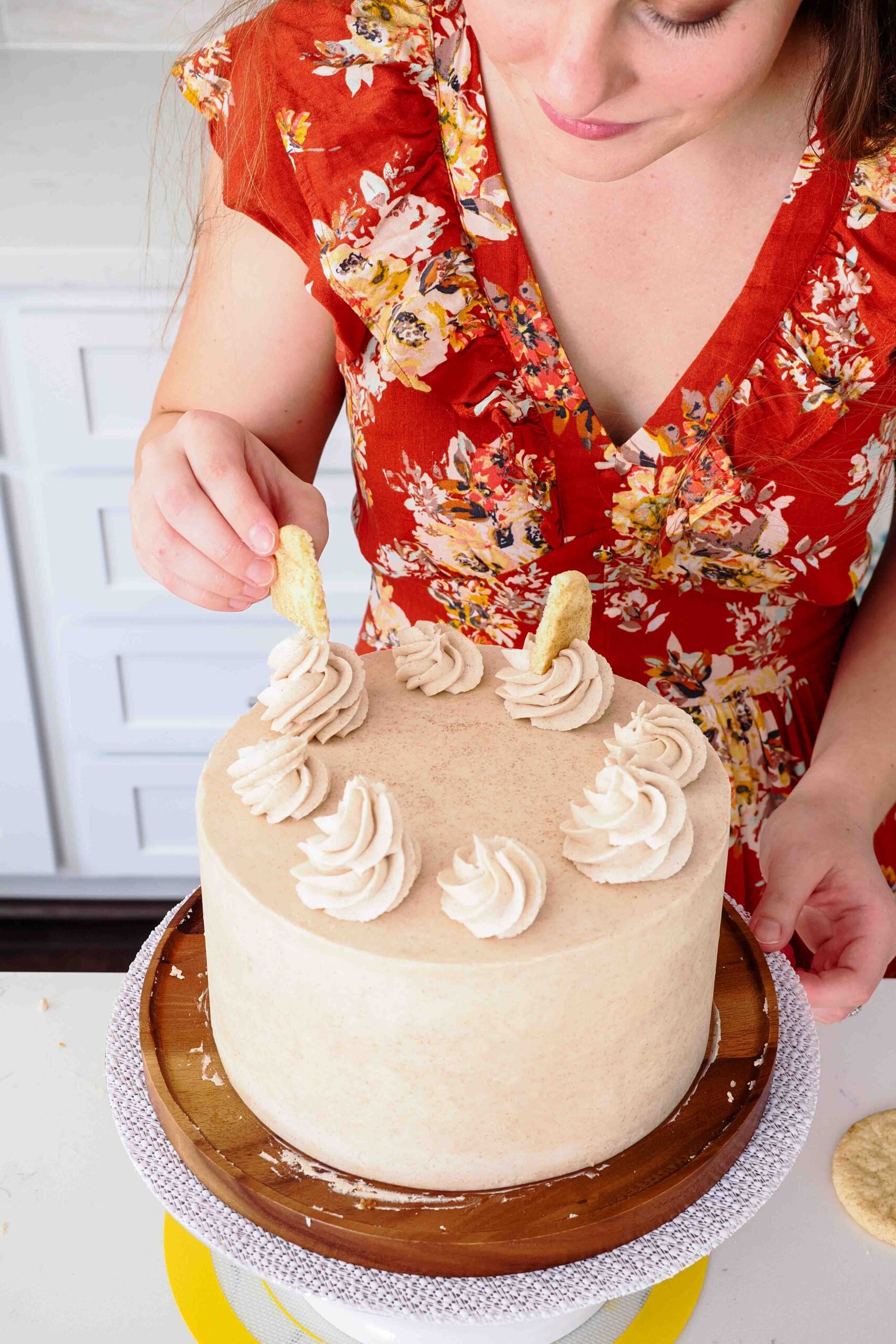 A woman adds wedges of snickerdoodle cookies on top of a cake.
