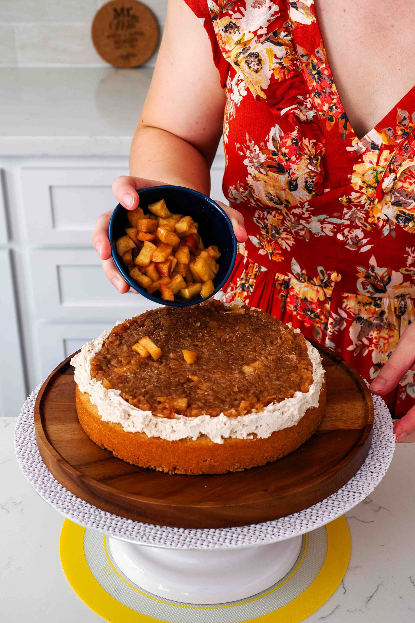 A woman sprinkles cooked apple pieces on top of a spiced apple cake filling.