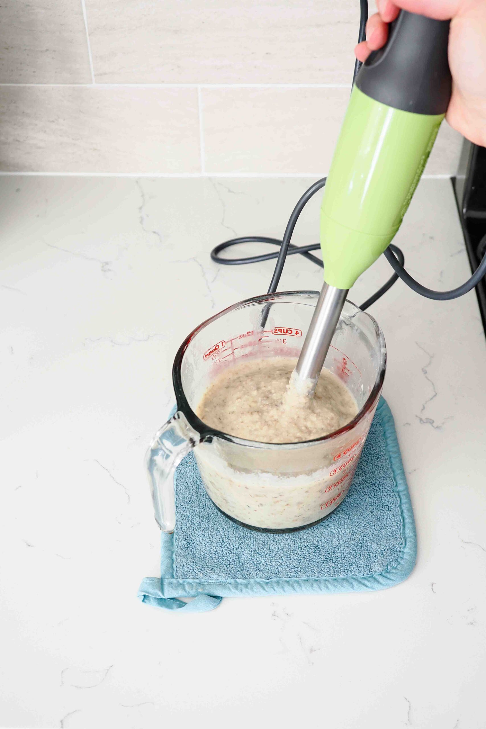 An immersion blender sticks out of a measuring cup with thick, blended soup.