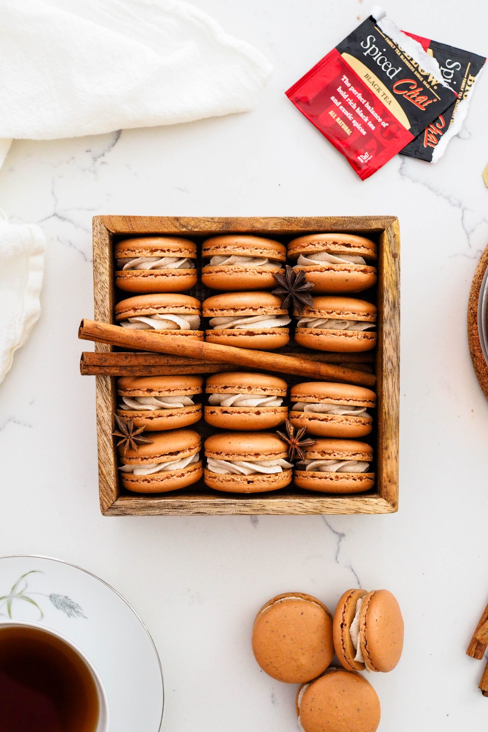Chai macarons in a wooden box with cinnamon sticks and star anise.