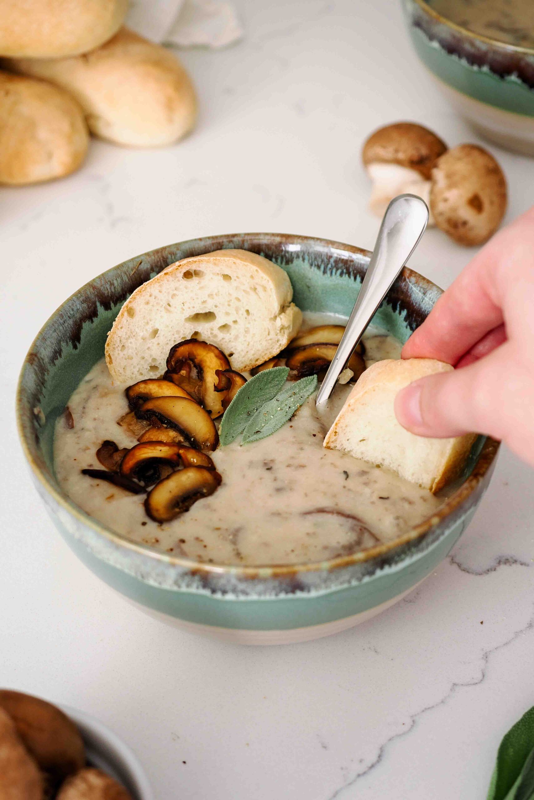 A hand dips a slice of bread into mushroom potato soup.