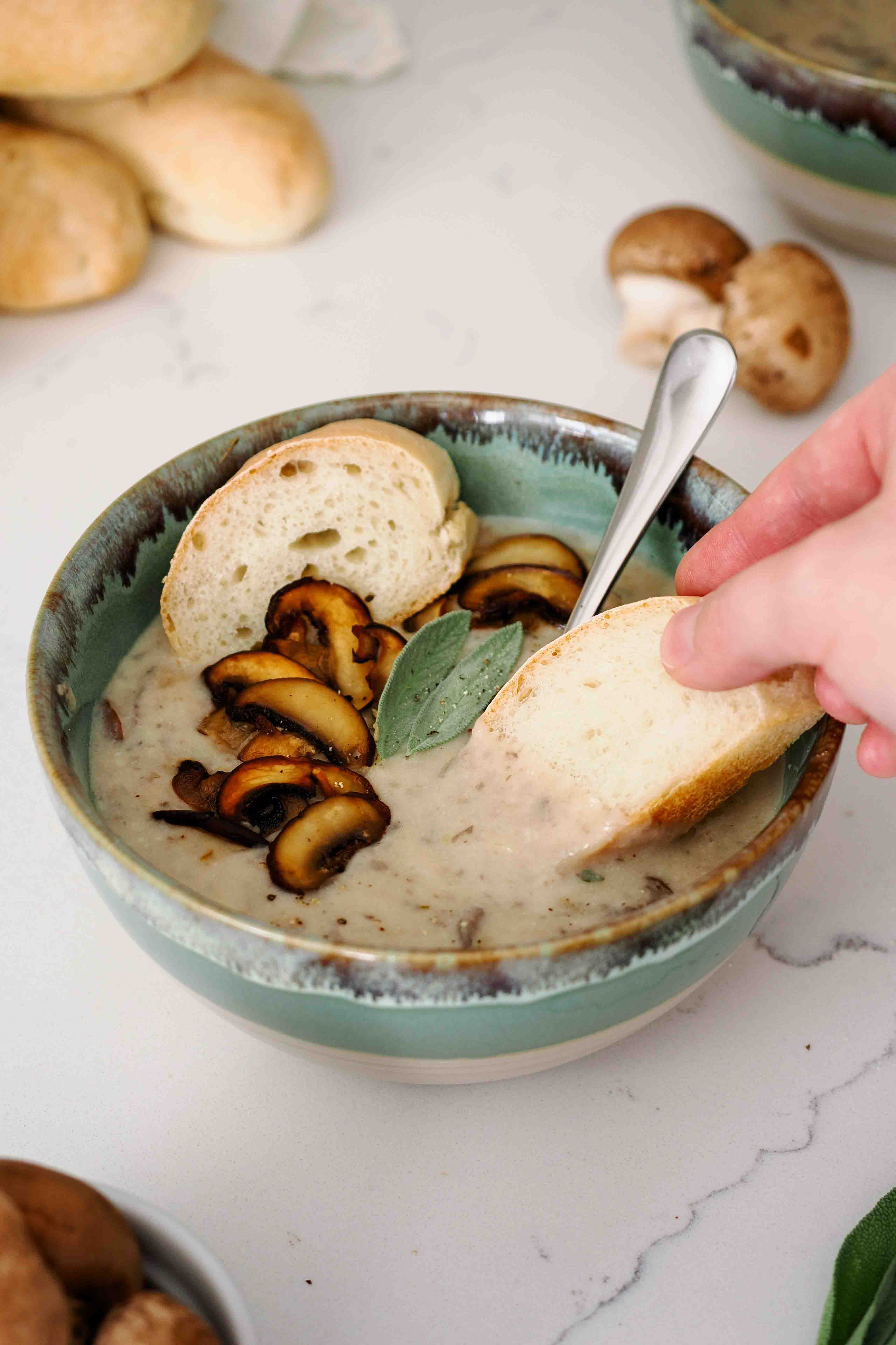 A hand dips a slice of bread into mushroom potato soup.