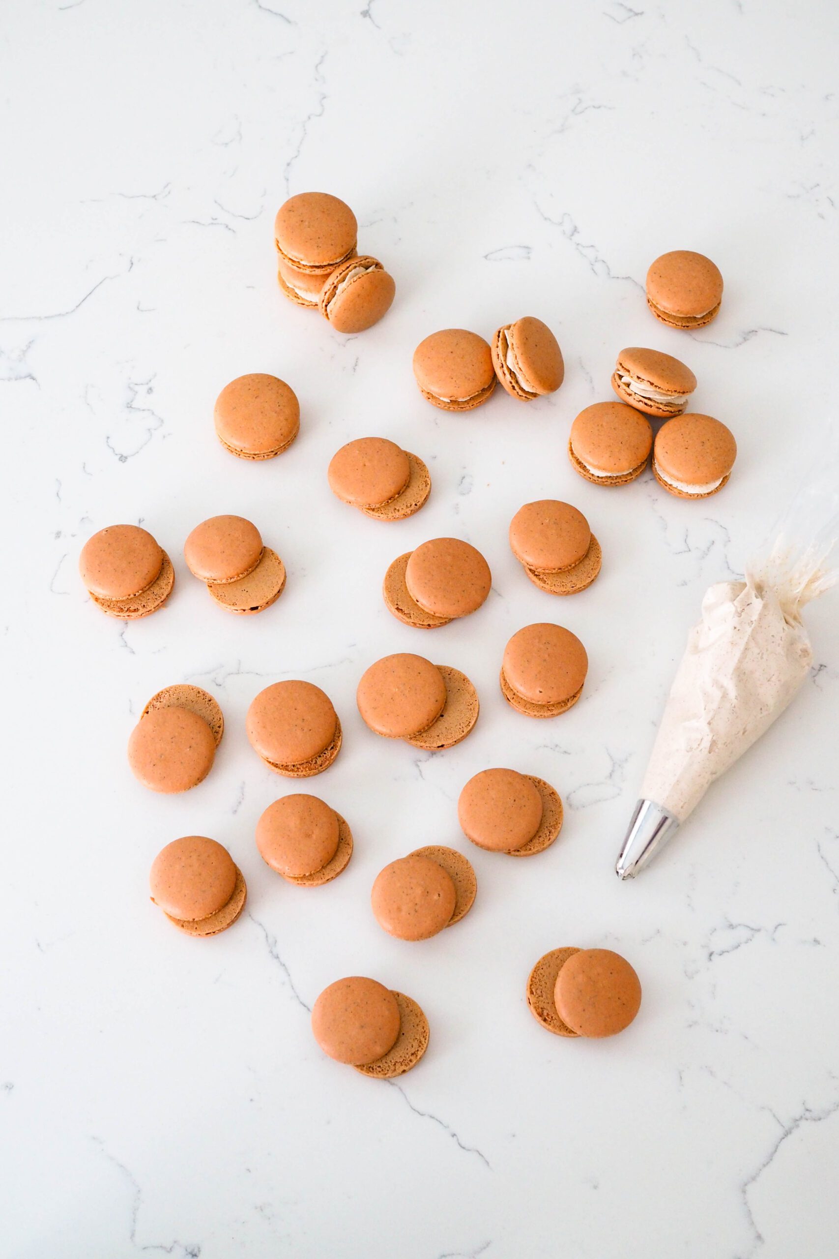 Paired macarons on a quartz counter with a bag of chai buttercream nearby.
