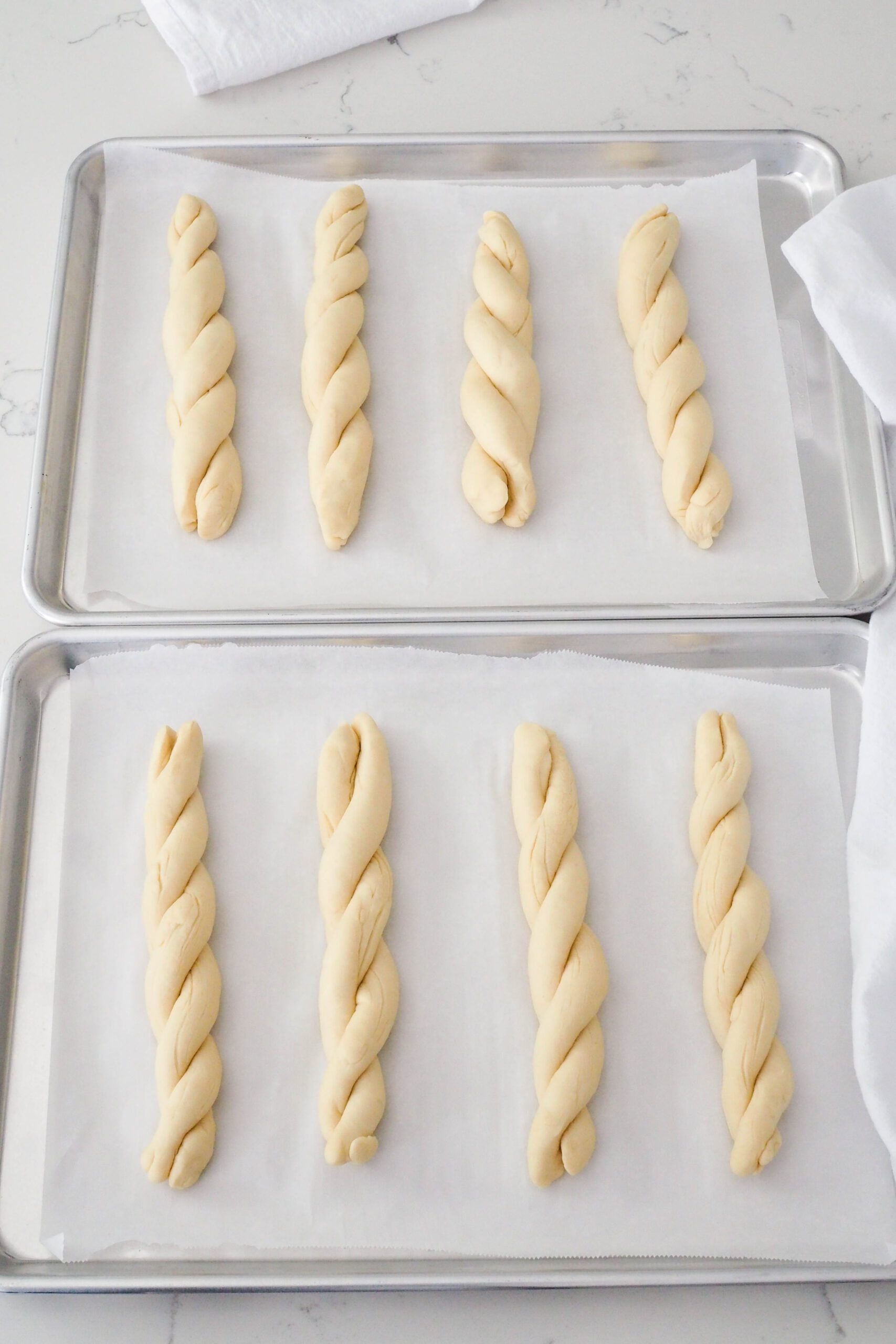 Eight proofed twisted garlic breadsticks on two baking sheets.