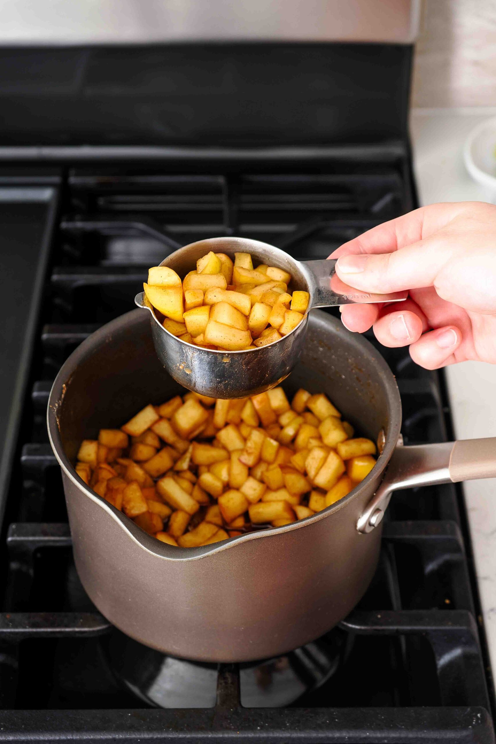 One cup of cooked and spiced apple pieces is removed from a pot.