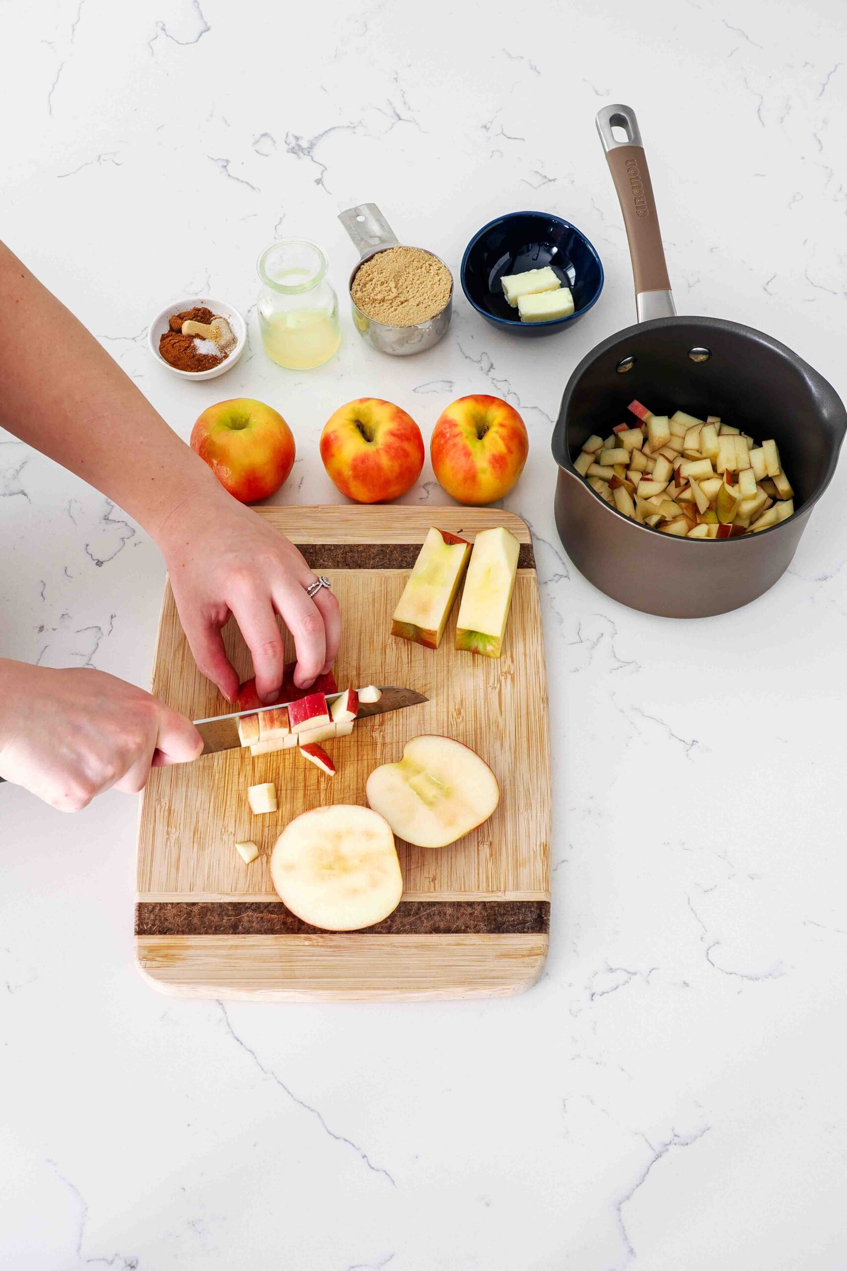 Two hands slice apples on a cutting board.