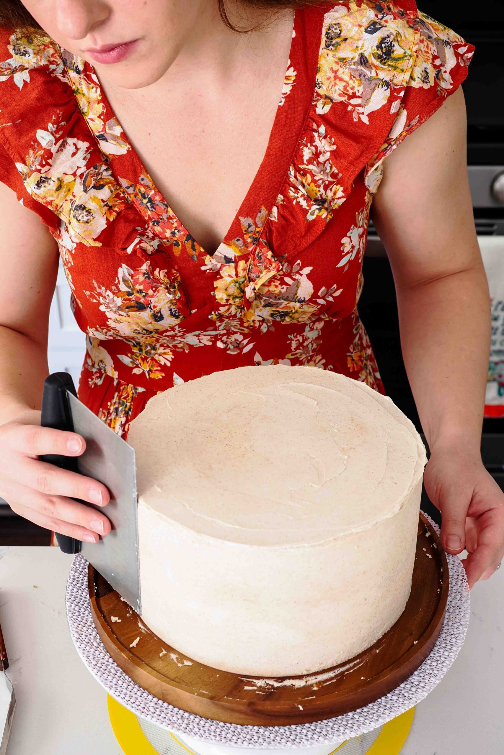 A woman smooths the sides of a cake frosted with cinnamon buttercream.