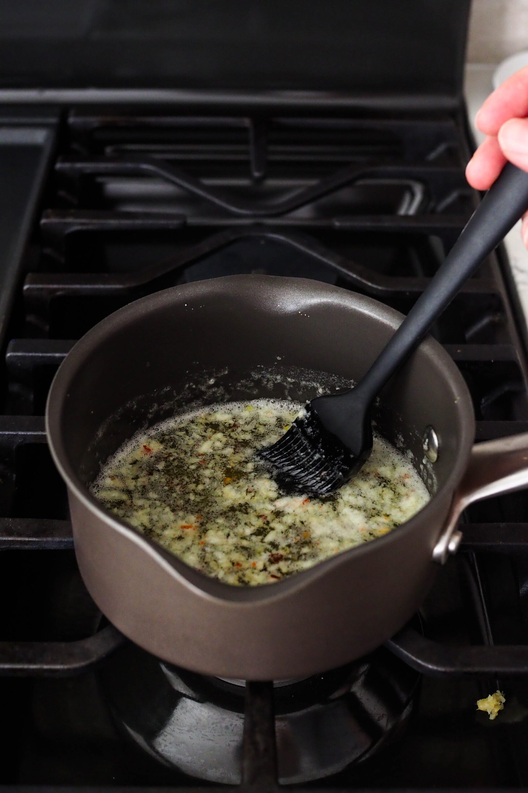 A pastry brush stirs garlic into butter in a small saucepan.
