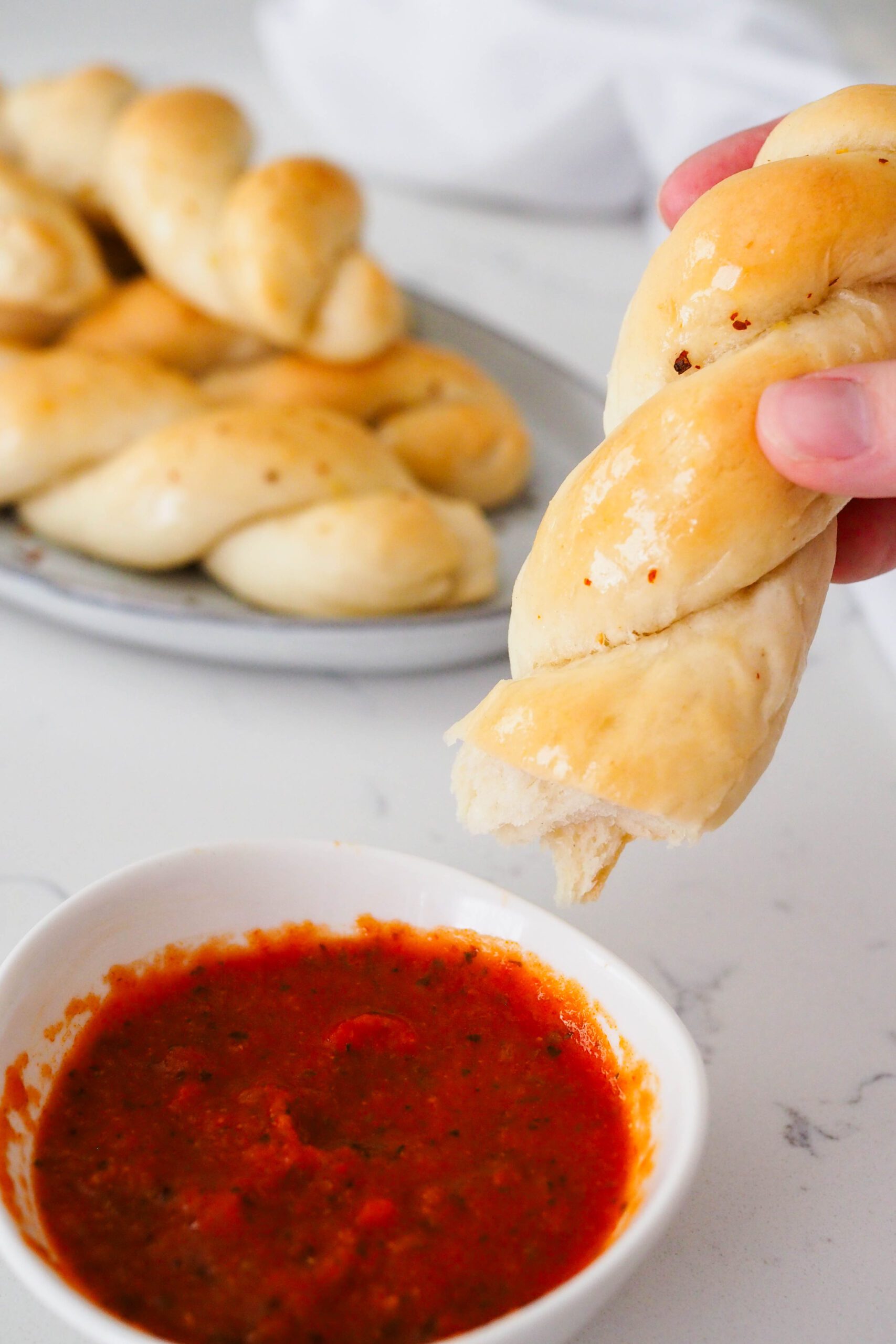 Half of a twisted garlic breadstick is dipped into marinara sauce.