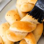 A silicone pastry brush brushes garlic butter onto twisted breadsticks.