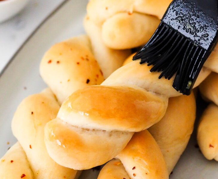A silicone pastry brush brushes garlic butter onto twisted breadsticks.