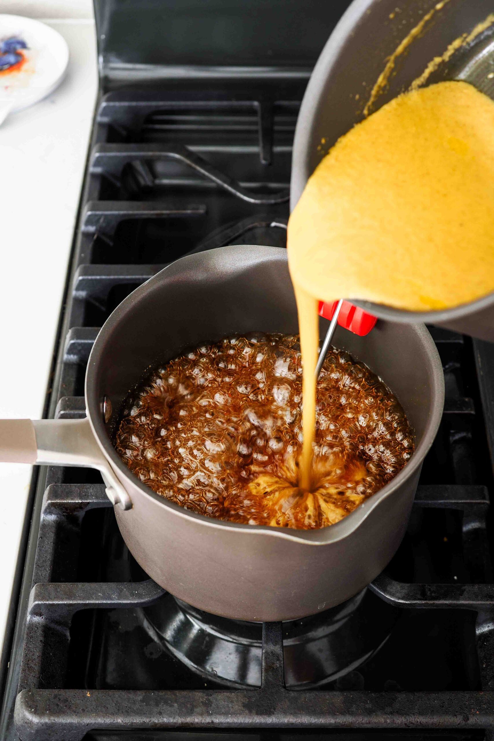 Pumpkin cream is poured into a pot of caramel over the stove.