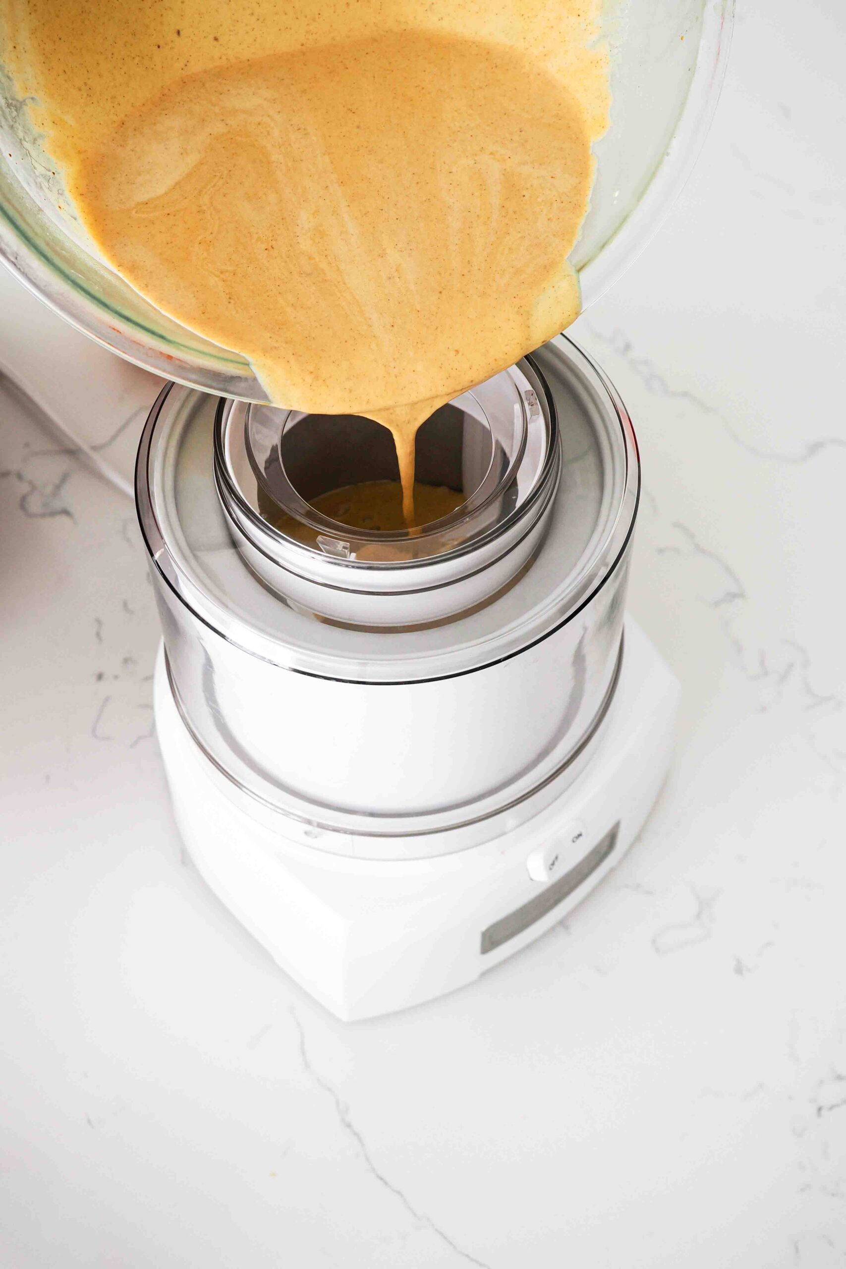 Pumpkin custard is poured into an ice cream maker canister.