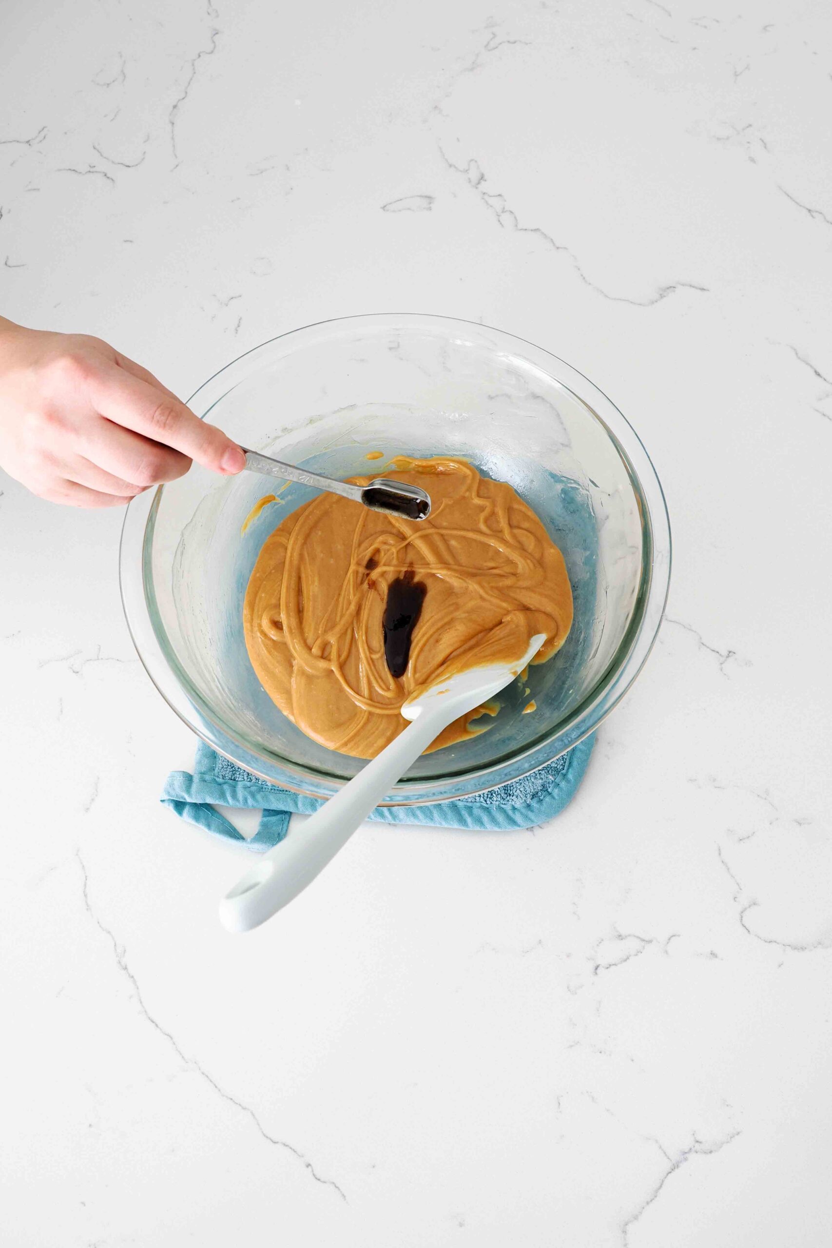 Vanilla extract is poured into a large glass bowl with a peanut butter mixture.