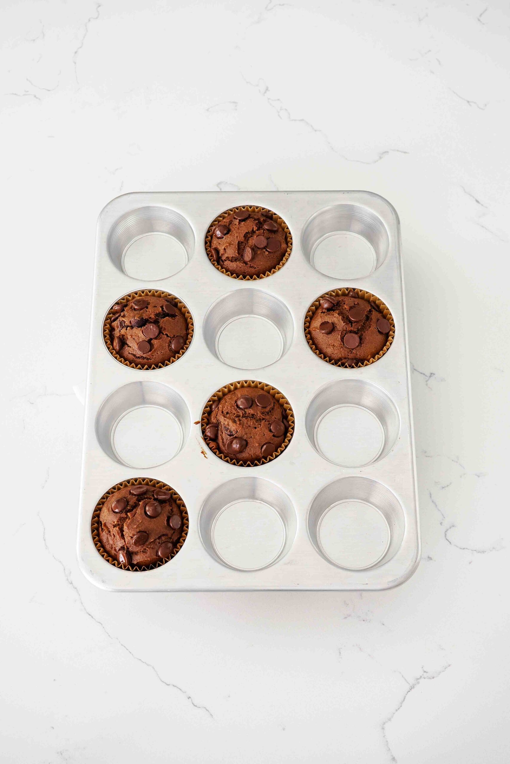 Fully baked chocolate pumpkin muffins in an aluminum muffin pan.