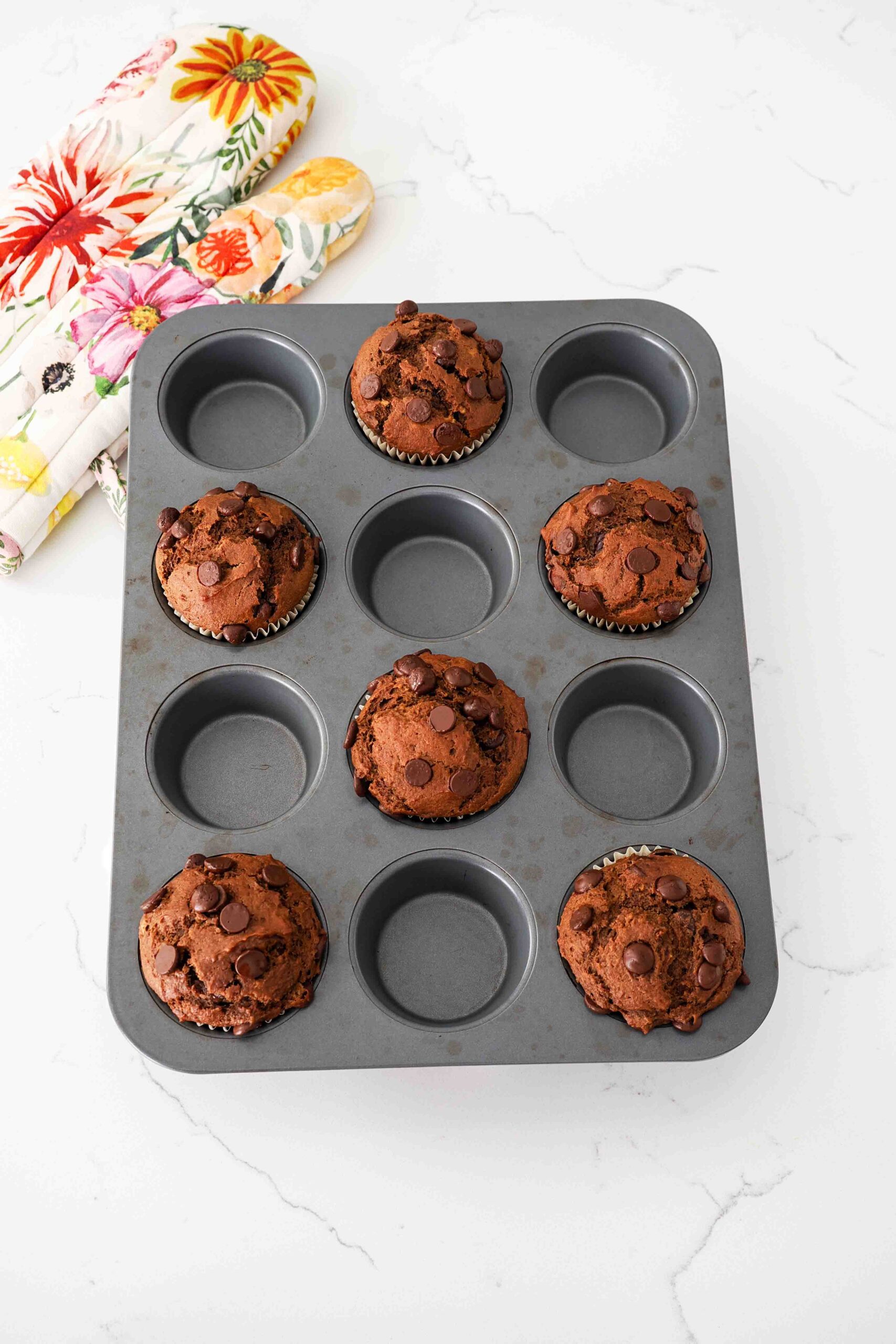 Fully baked large chocolate pumpkin muffins in a dark muffin pan.