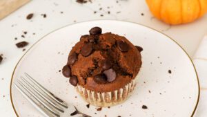 A closeup of a chocolate pumpkin muffin with a pumpkin in the background.