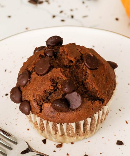 A closeup of a chocolate pumpkin muffin with a pumpkin in the background.