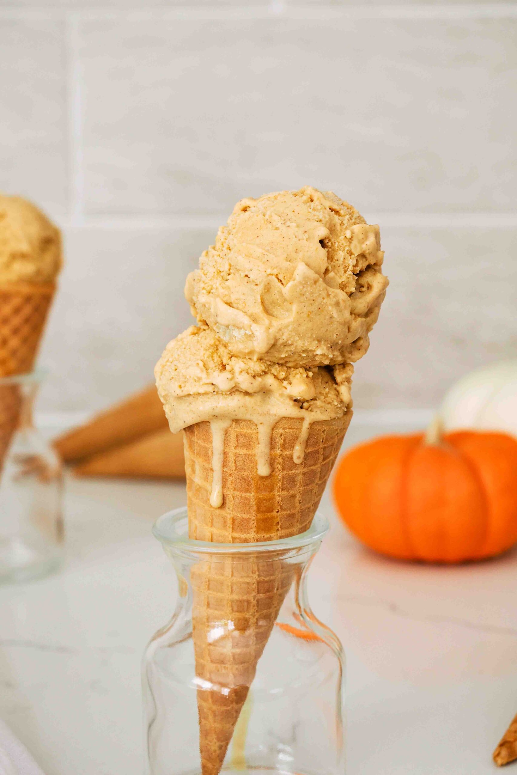 A closeup of an ice cream cone with two scoops of pumpkin pie ice cream.