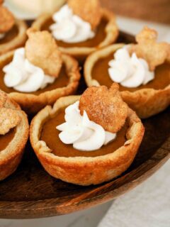 A closeup of a mini pumpkin pie with a swirl of whipped cream and a sugared pie crust pumpkin on top.
