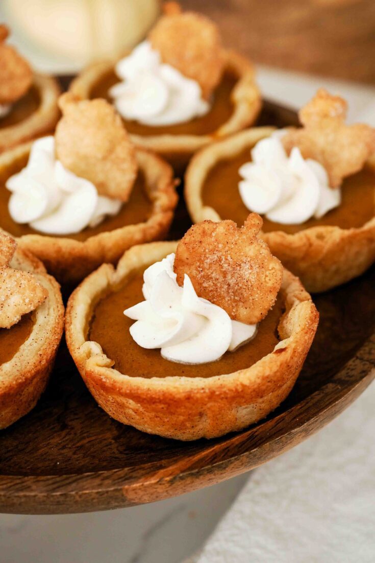 A closeup of a mini pumpkin pie with a swirl of whipped cream and a sugared pie crust pumpkin on top.