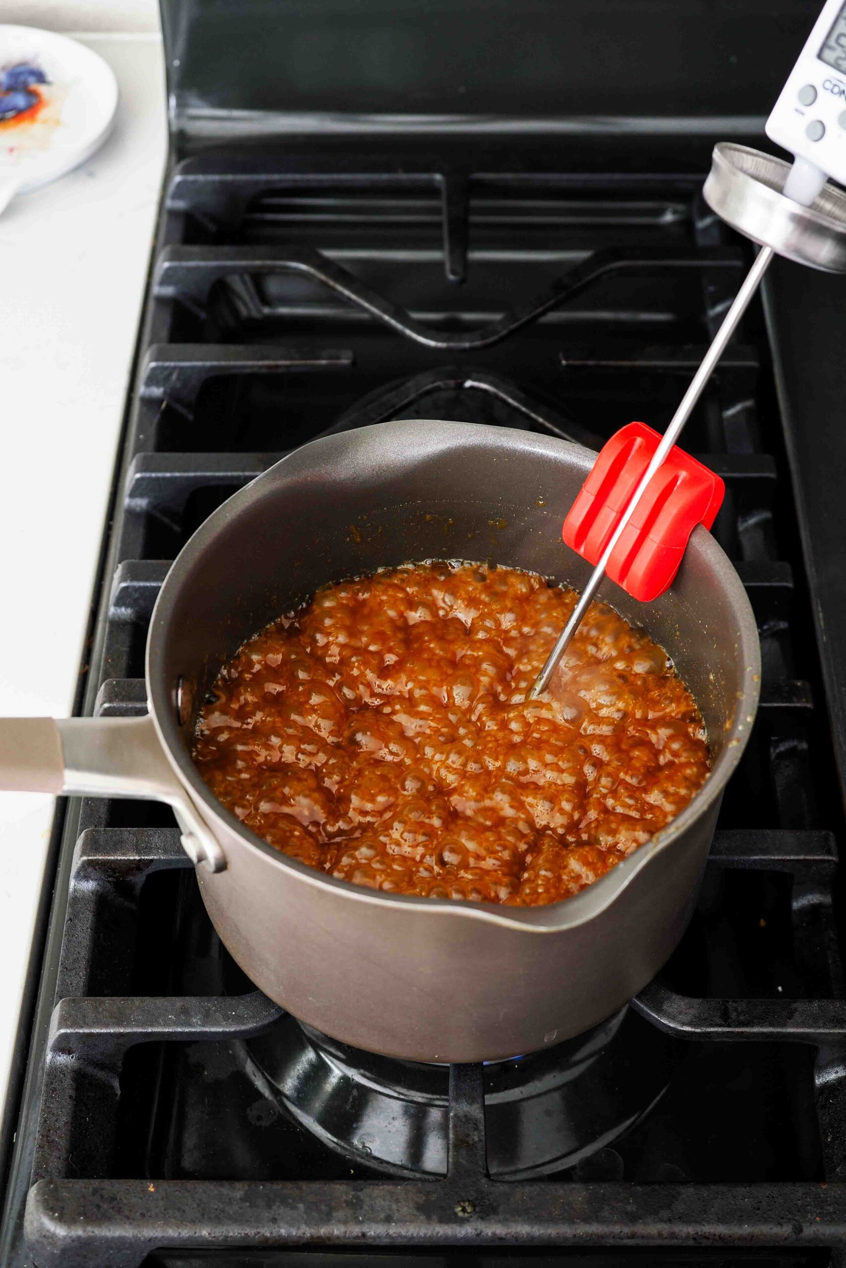 A pot of caramel over the stove with a candy thermometer.