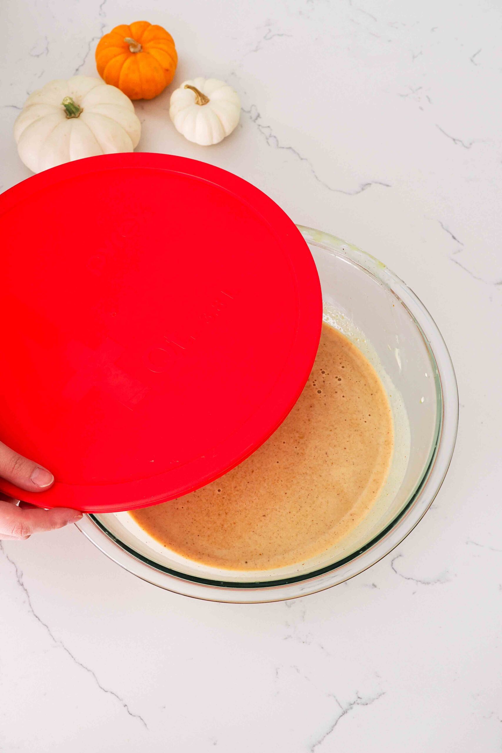 A hand adds a bright red lid over a large bowl with pumpkin custard.
