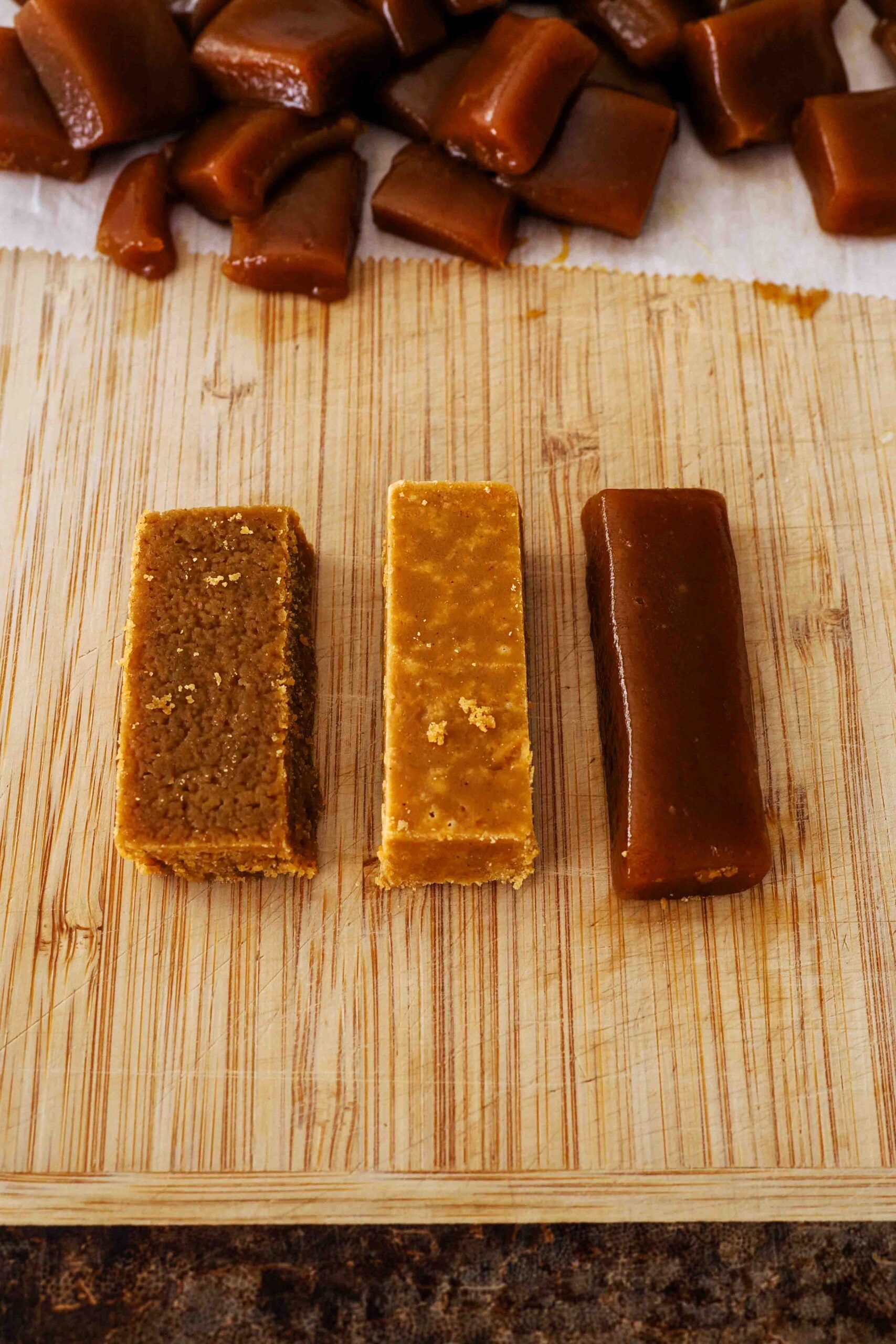 Three caramels on a cutting board: The two leftmost caramels are grainy and crystallized, and the caramel on the right is dark and shiny.