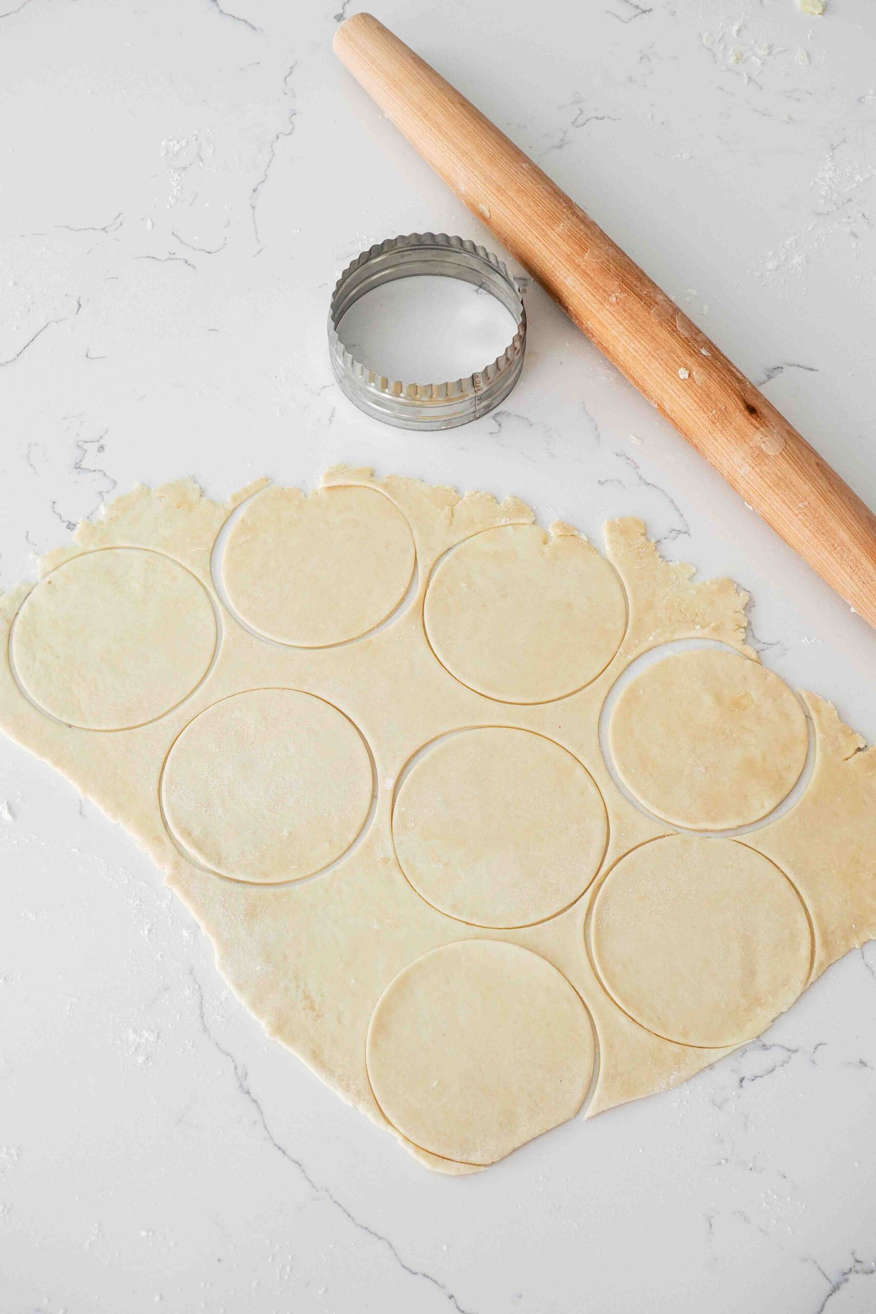 A round cutter near rolled out pie crust and a rolling pin.