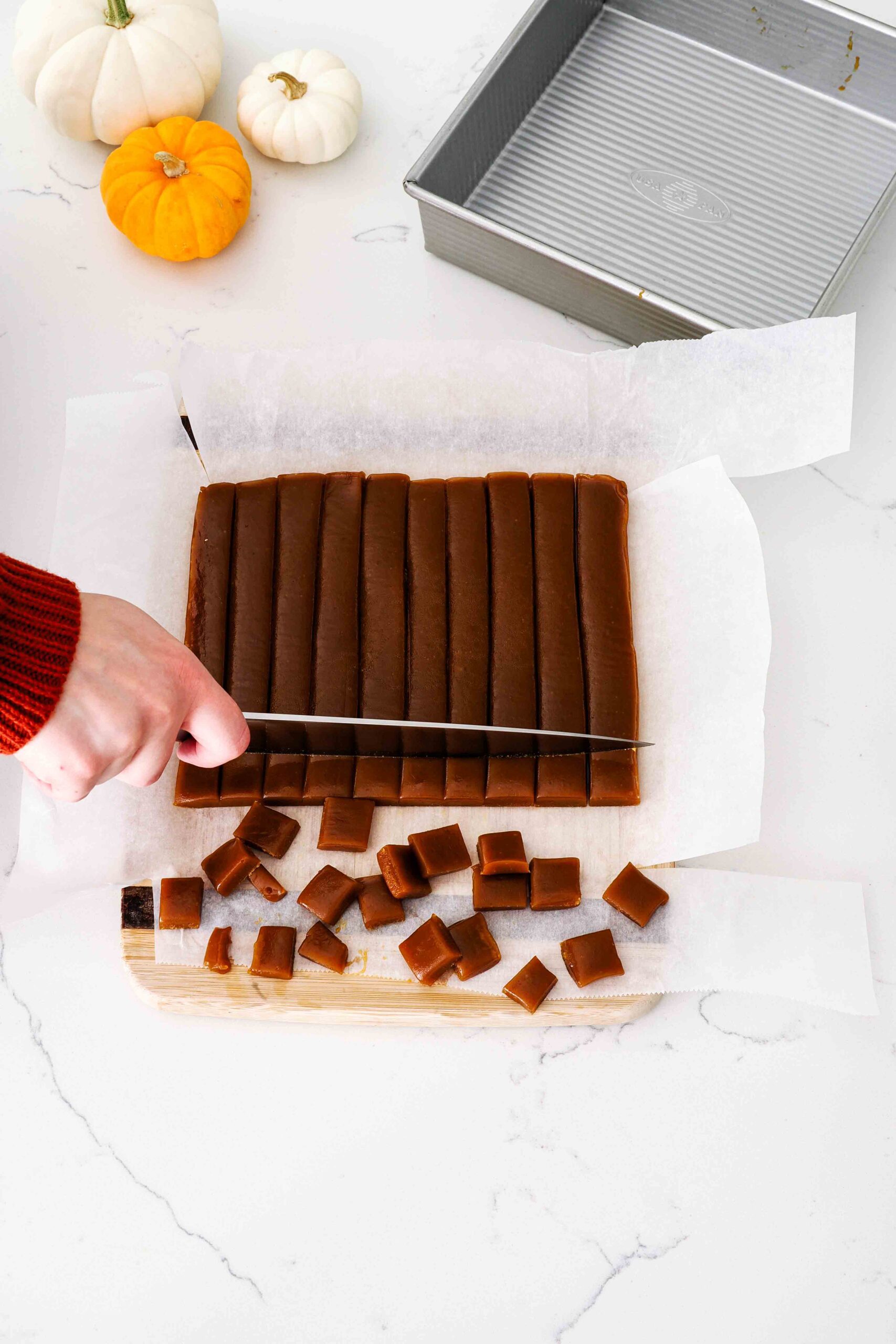 A knife cuts individual caramel candies out of a slab of pumpkin spice caramel.