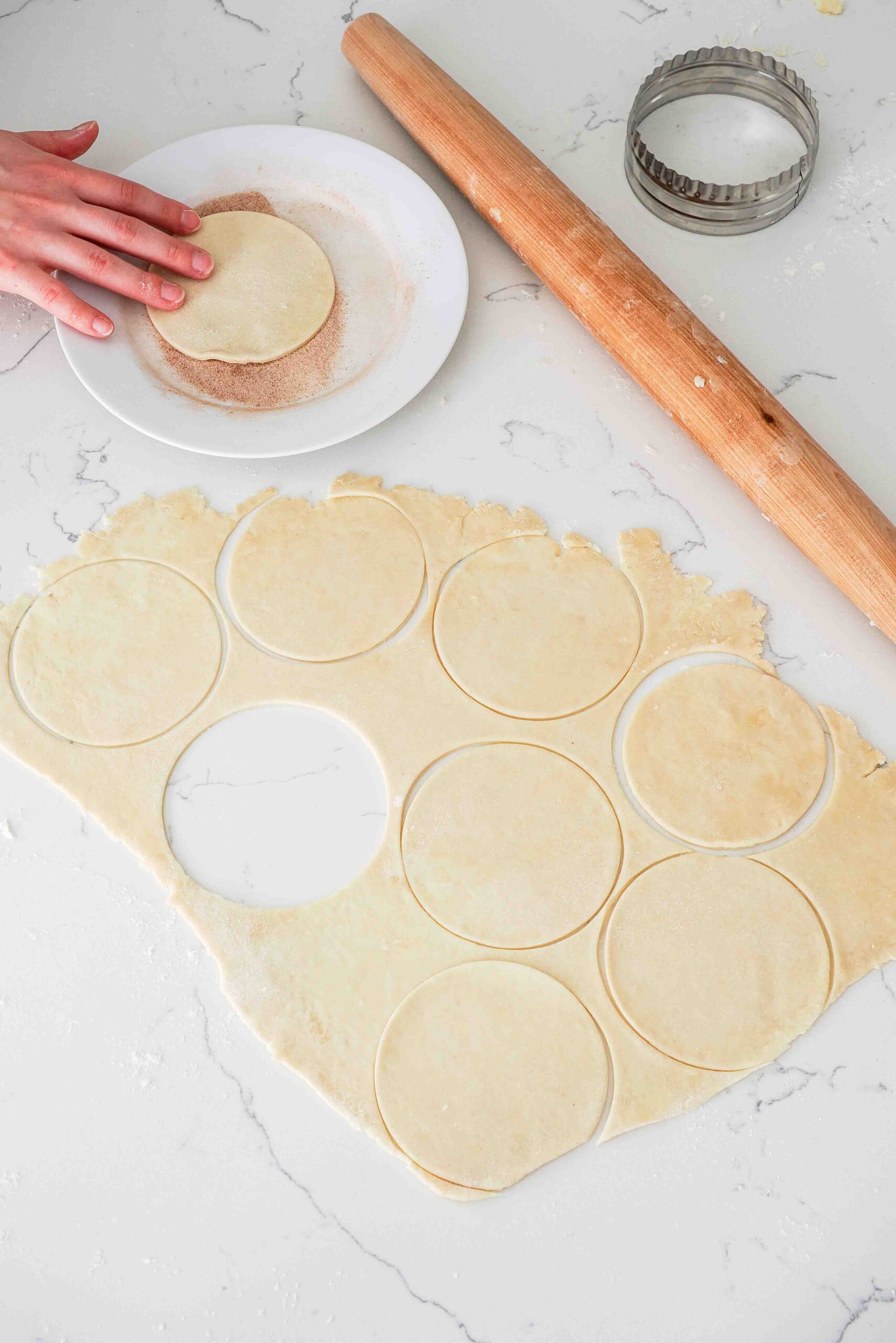 A hand dips a round of pie dough into cinnamon sugar.