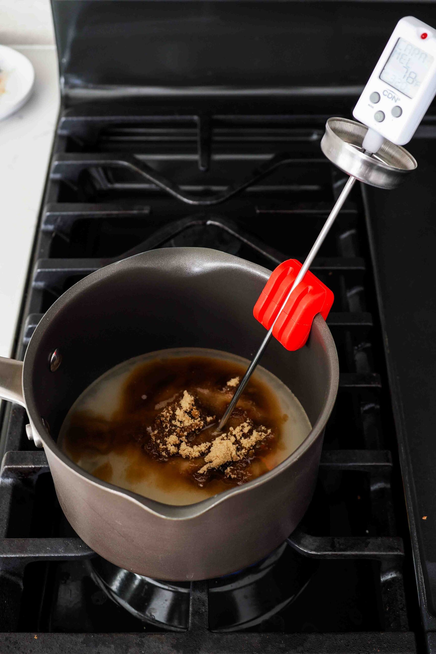 Unmixed sugar, brown sugar, and corn syrup in a pot over the stove with a candy thermometer.