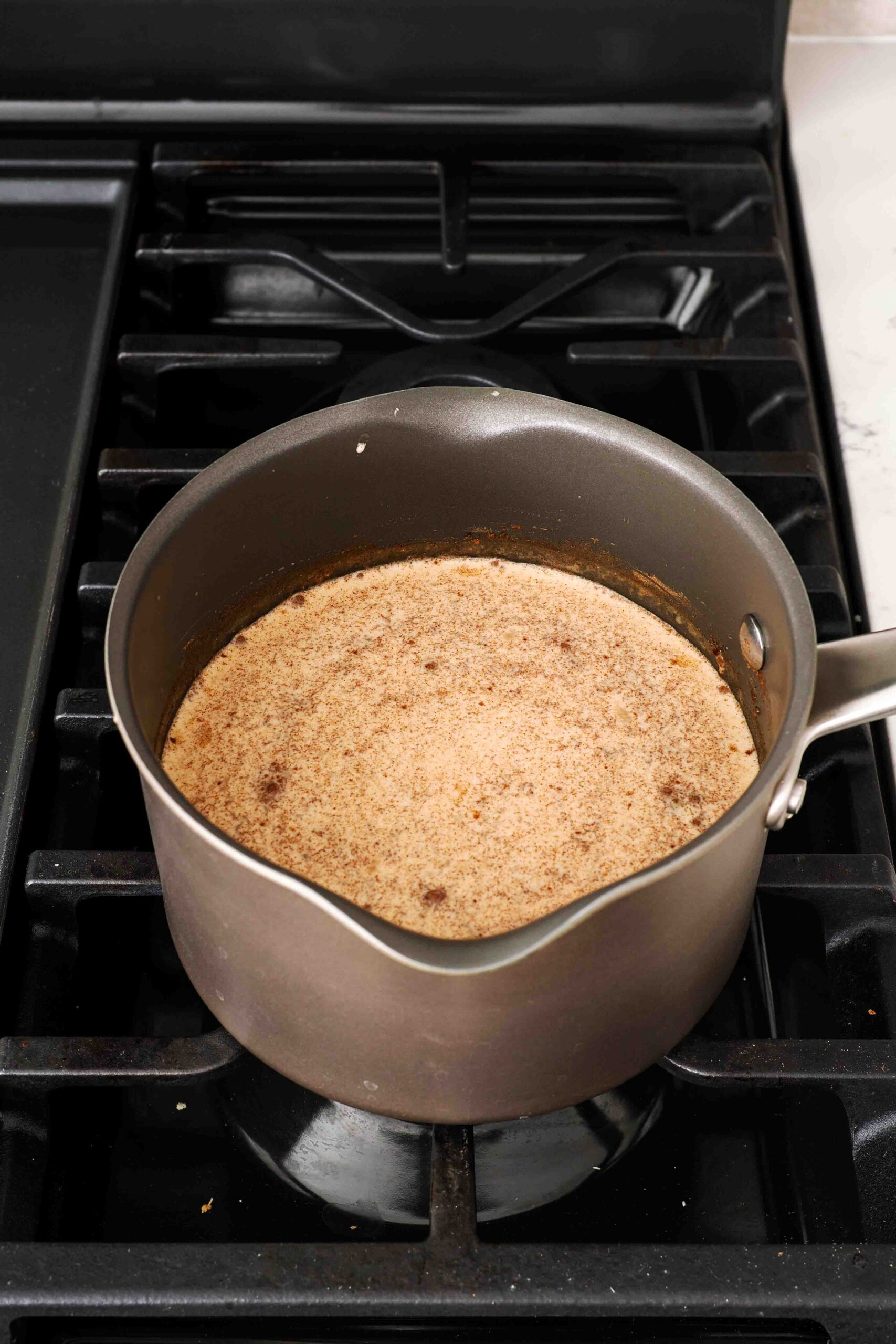 Orange-brown pumpkin cream heats over the stove in a medium pot.