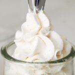 A piping tip pipes a swirl of whipped cream with vanilla bean speckles.