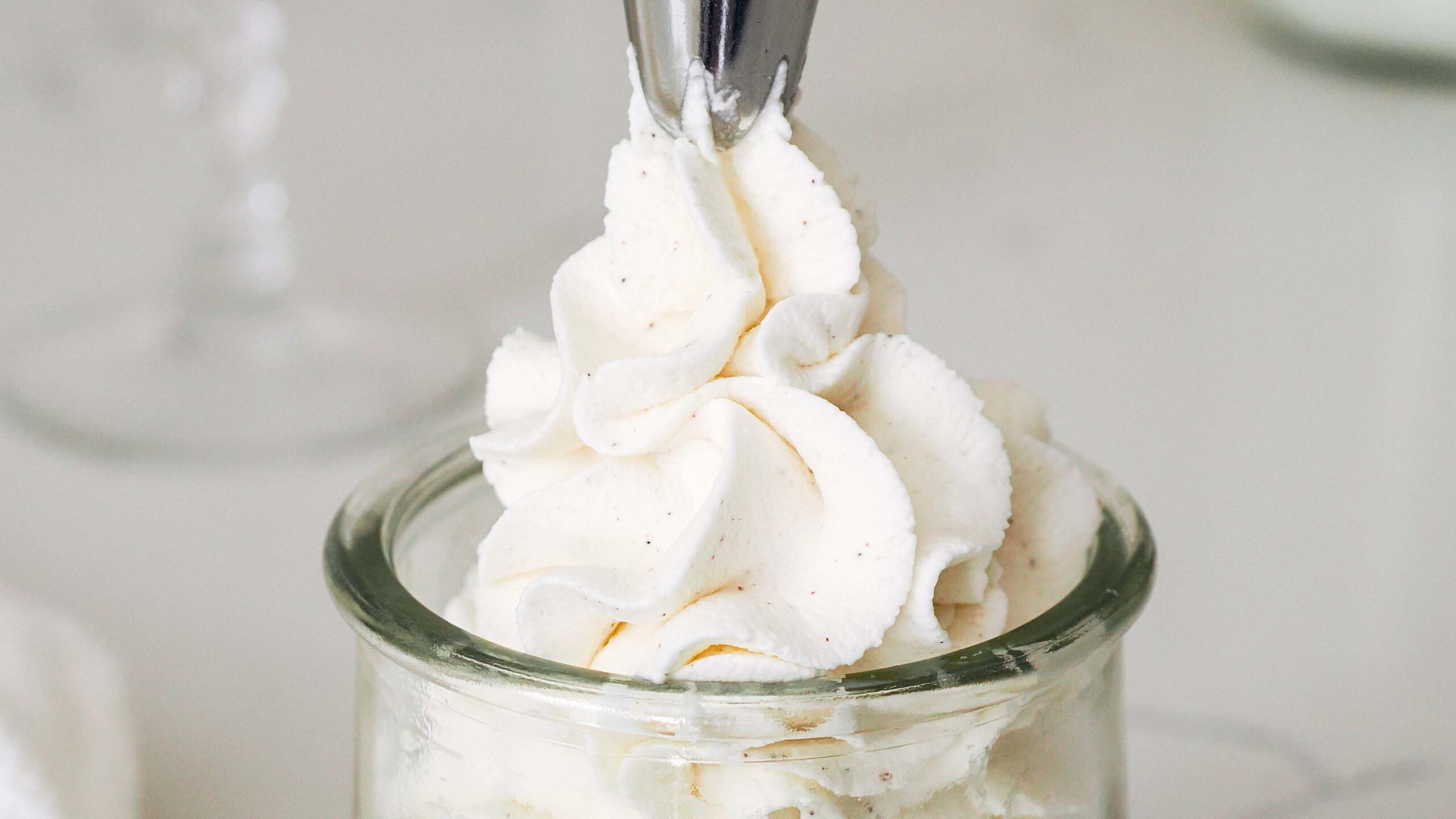 A piping tip pipes a swirl of whipped cream with vanilla bean speckles.