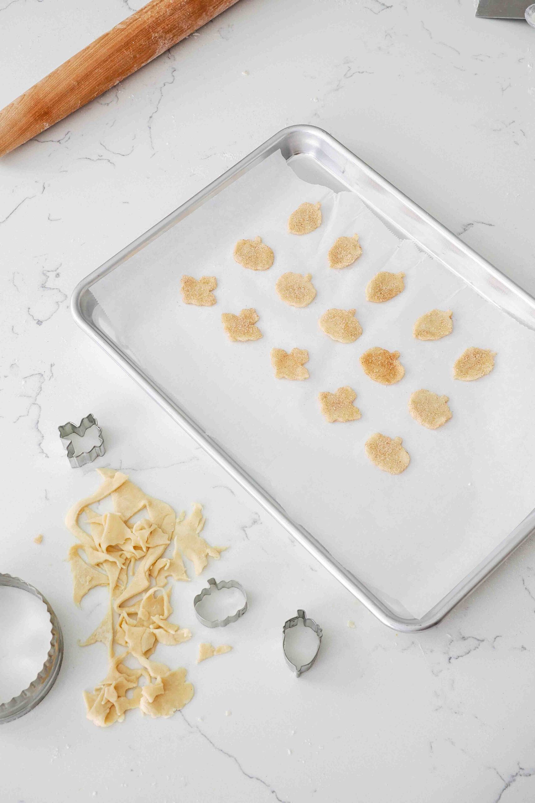 Small pieces of pie dough dusted with cinnamon sugar and cut into fall shapes on a baking sheet.