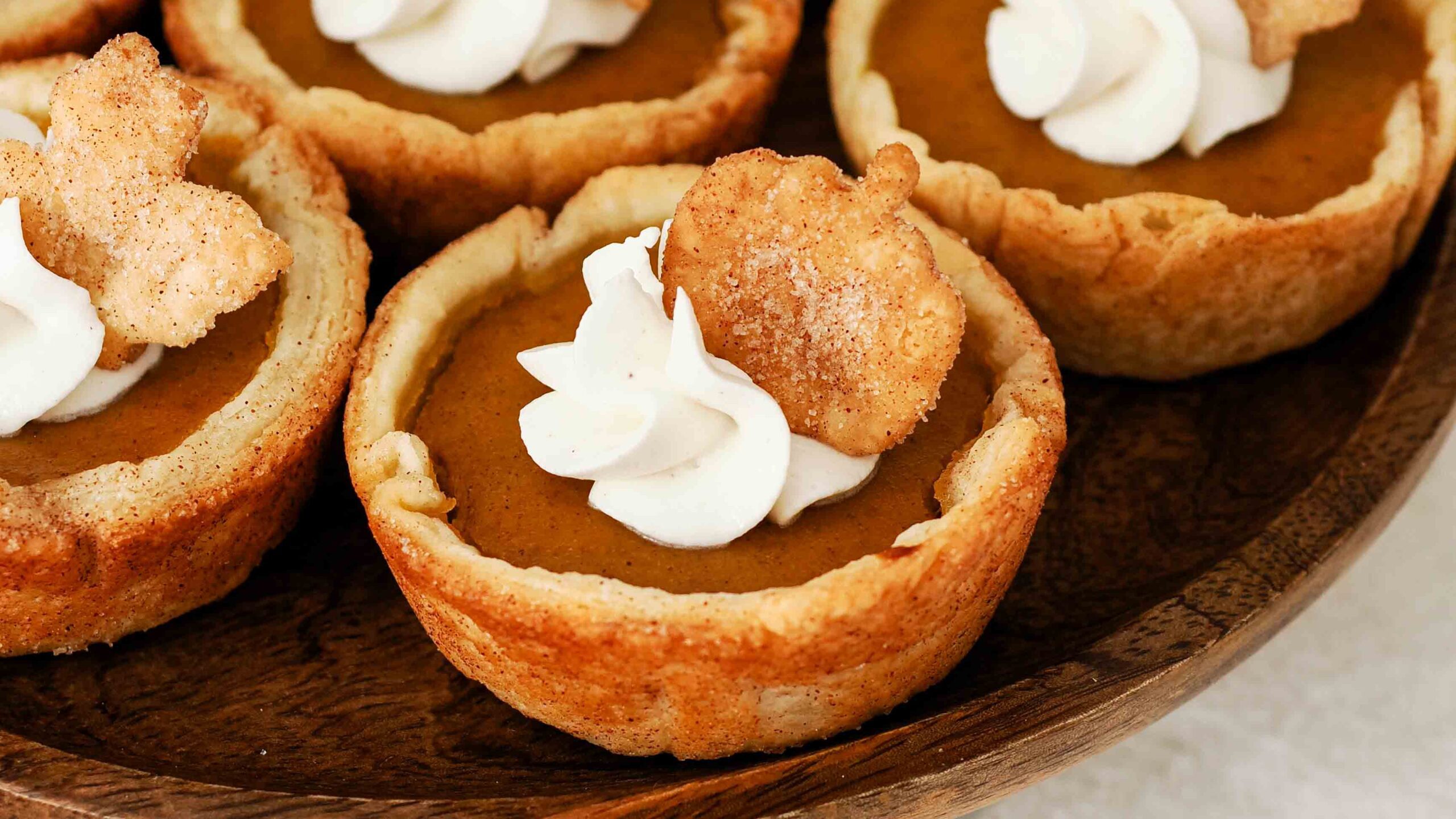 A closeup of a mini pumpkin pie with a swirl of whipped cream and a sugared pie crust pumpkin on top.