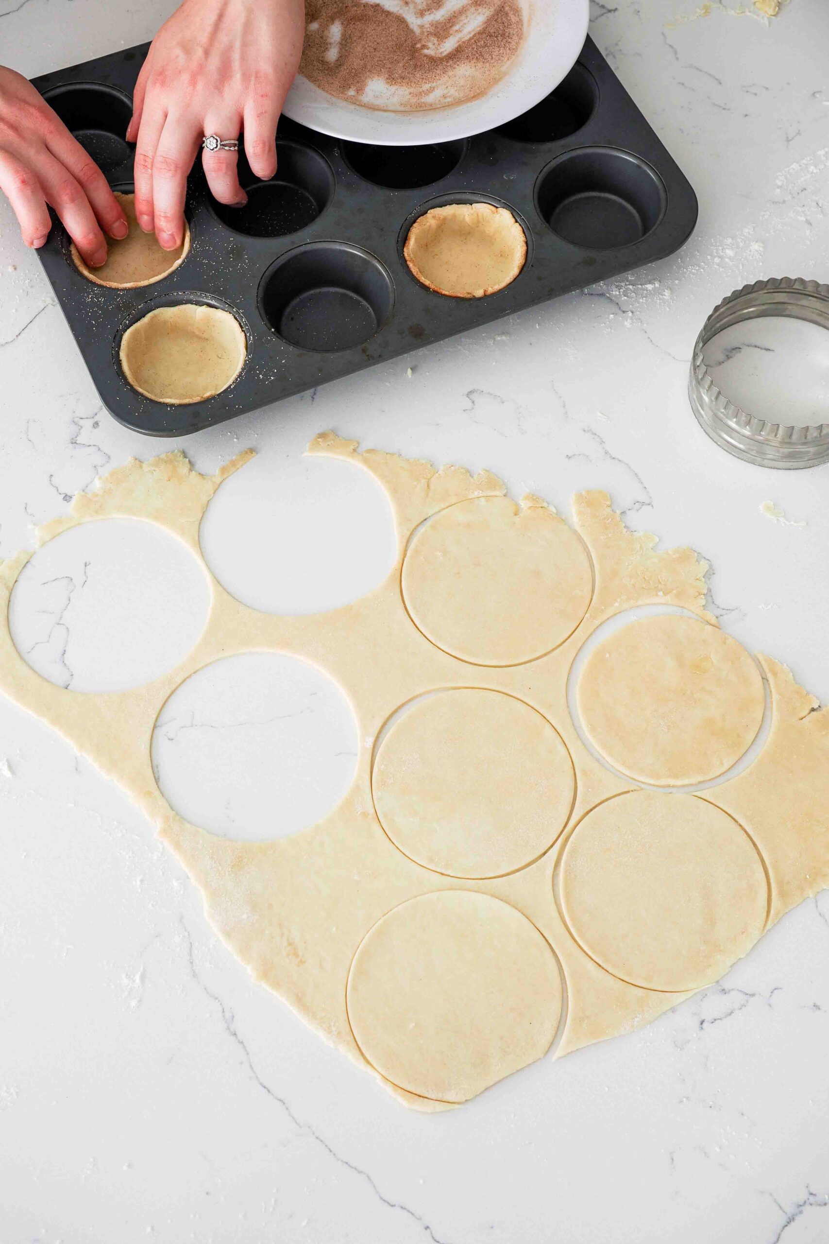 Two hands lightly press pie dough into a hole in a muffin pan.