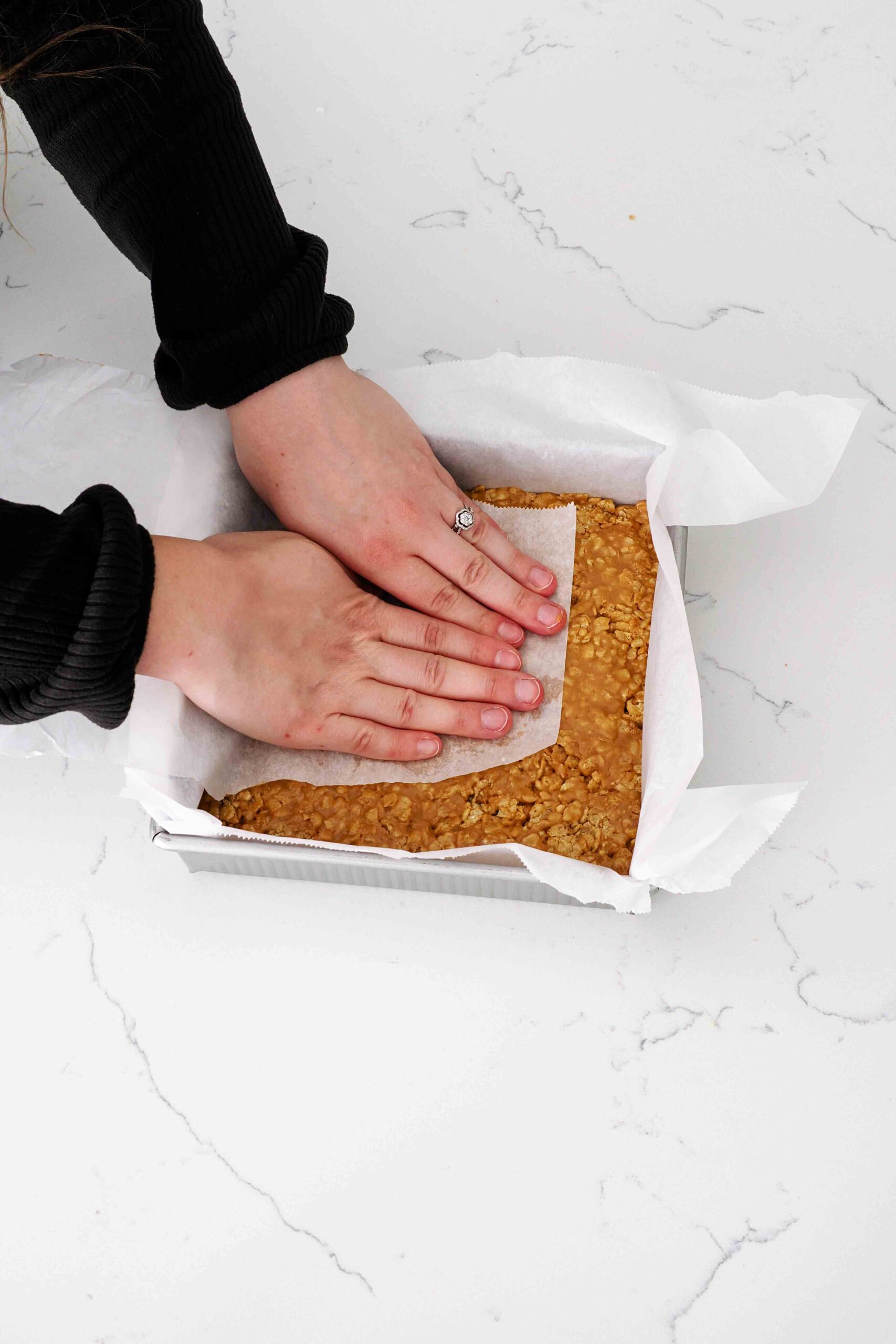 Two hands press Special K bars into a square pan with a piece of parchment paper.