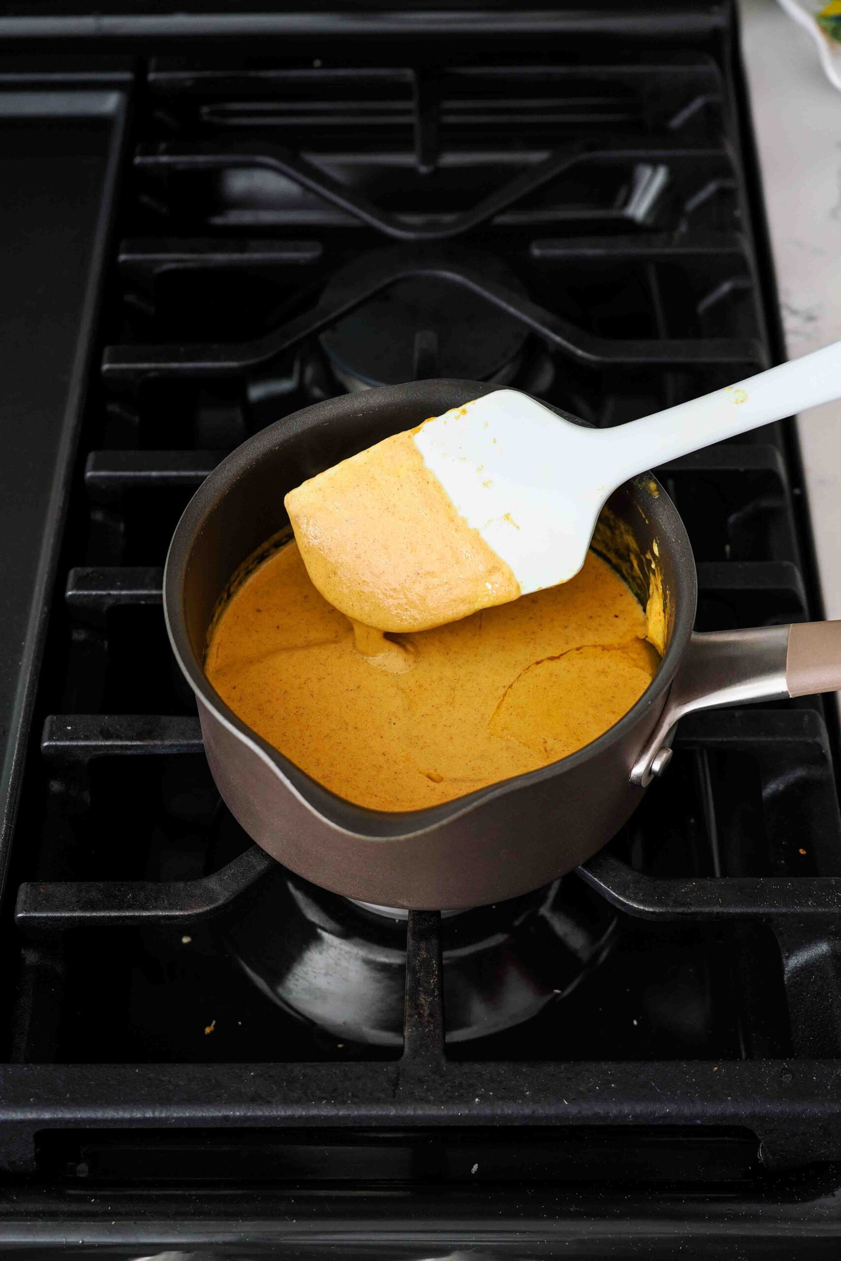 A spatula stirs together pumpkin cream over the stove.