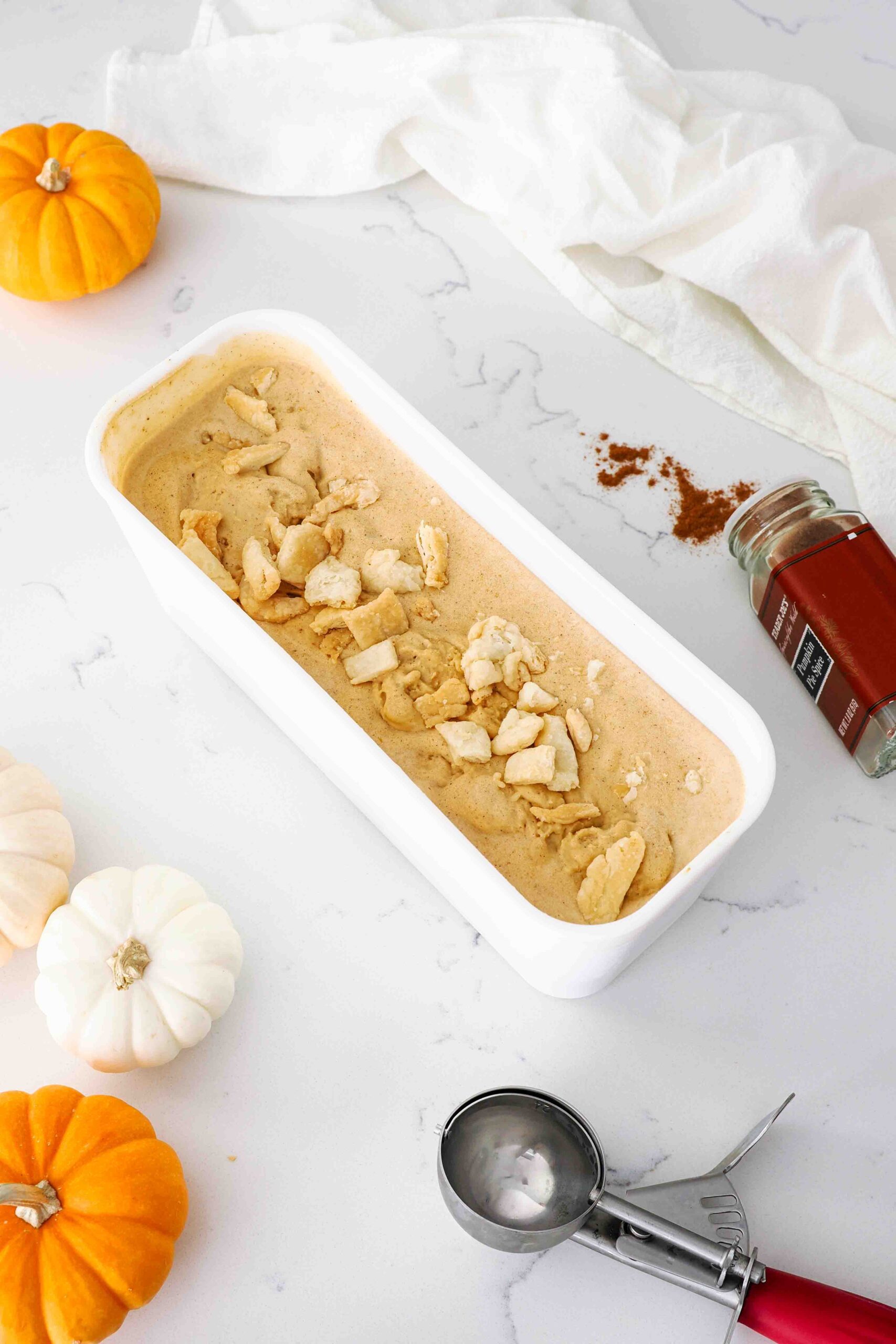 A container of pumpkin pie ice cream on a counter with mini pumpkins around it.