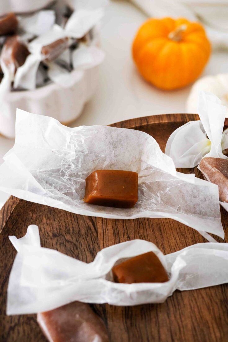 A pumpkin spice caramel rests on top of its wrapper with another nearby.