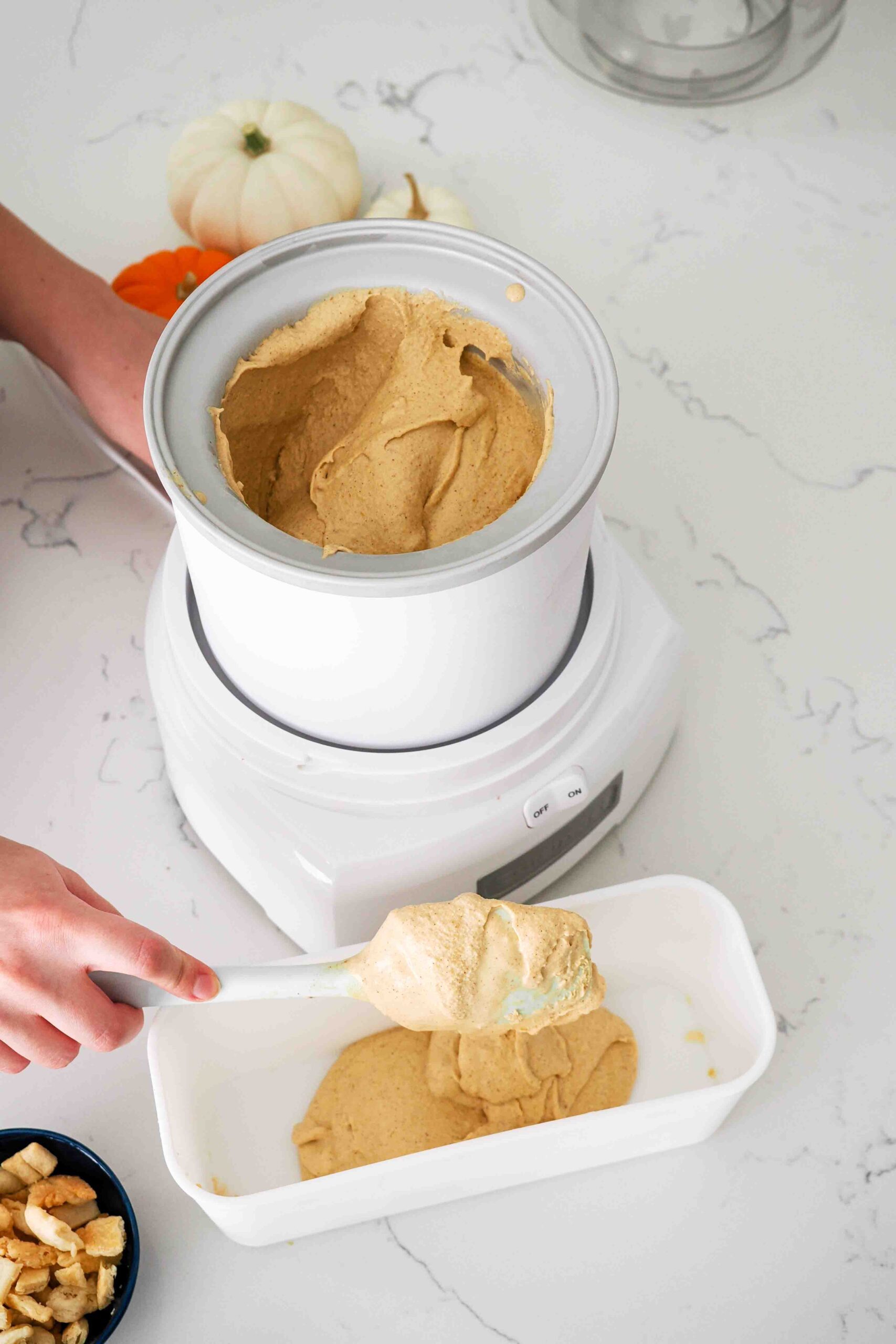 A spatula scoops ice cream out of an ice cream maker and into a storage container.