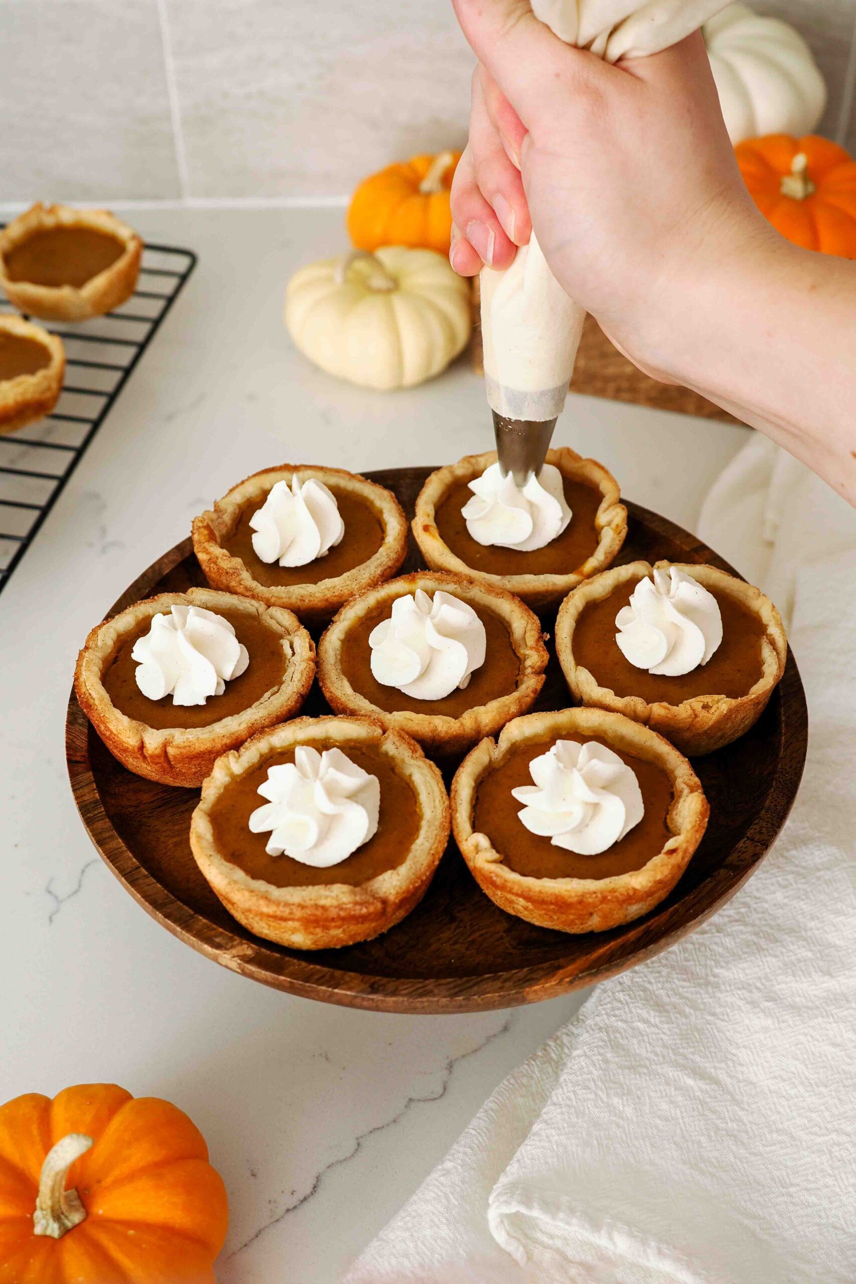 A hand pipes a dollop of whipped cream onto individual pumpkin pies.