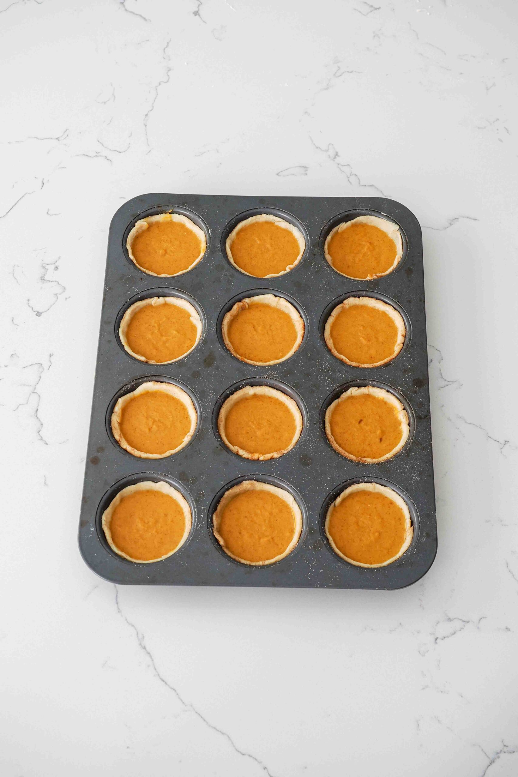 Unbaked mini pumpkin pies in a muffin pan.