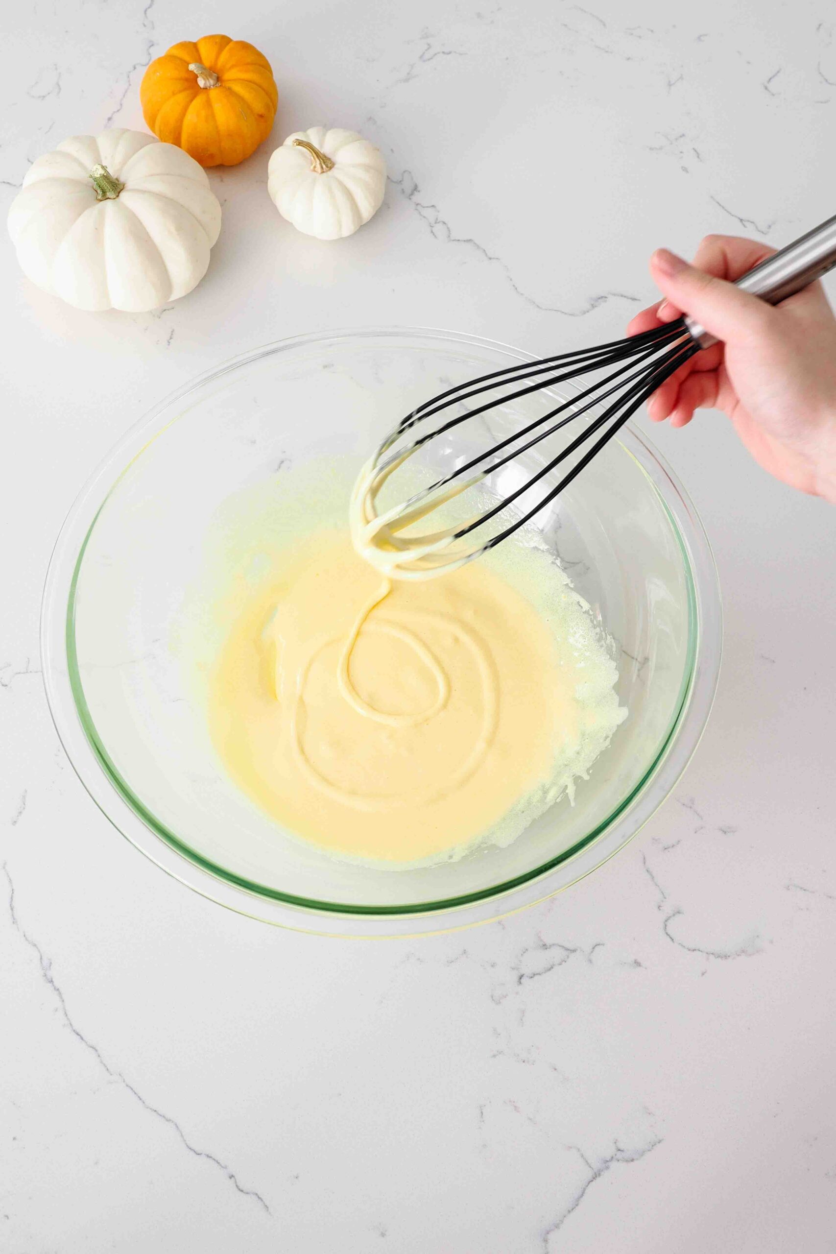 A whisk leaves a trail in a bowl of yolks and sugar.
