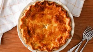 A dark golden brown pie on a cherry wood table with forks.
