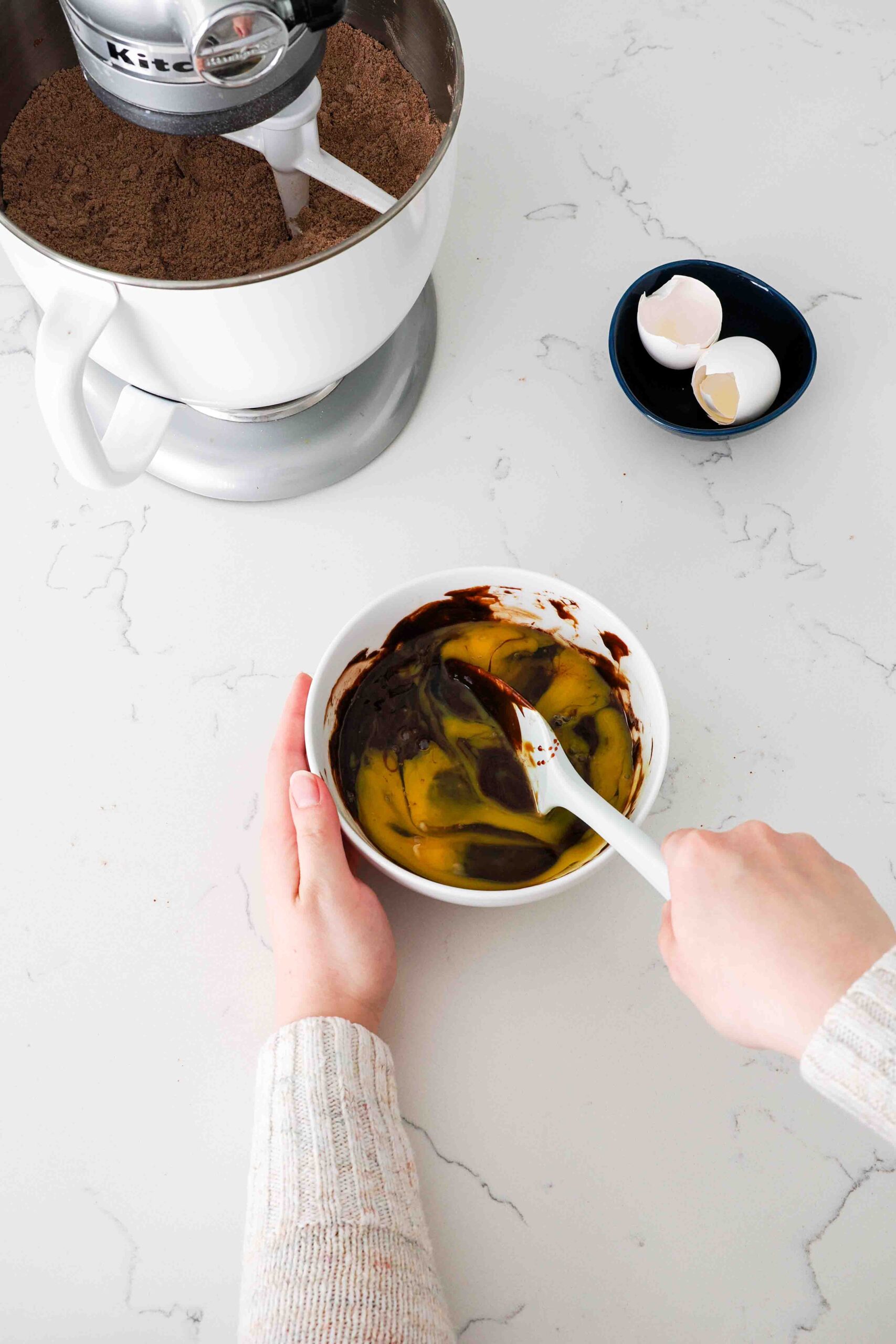 Two hands stir together eggs, molasses, and melted chocolate.