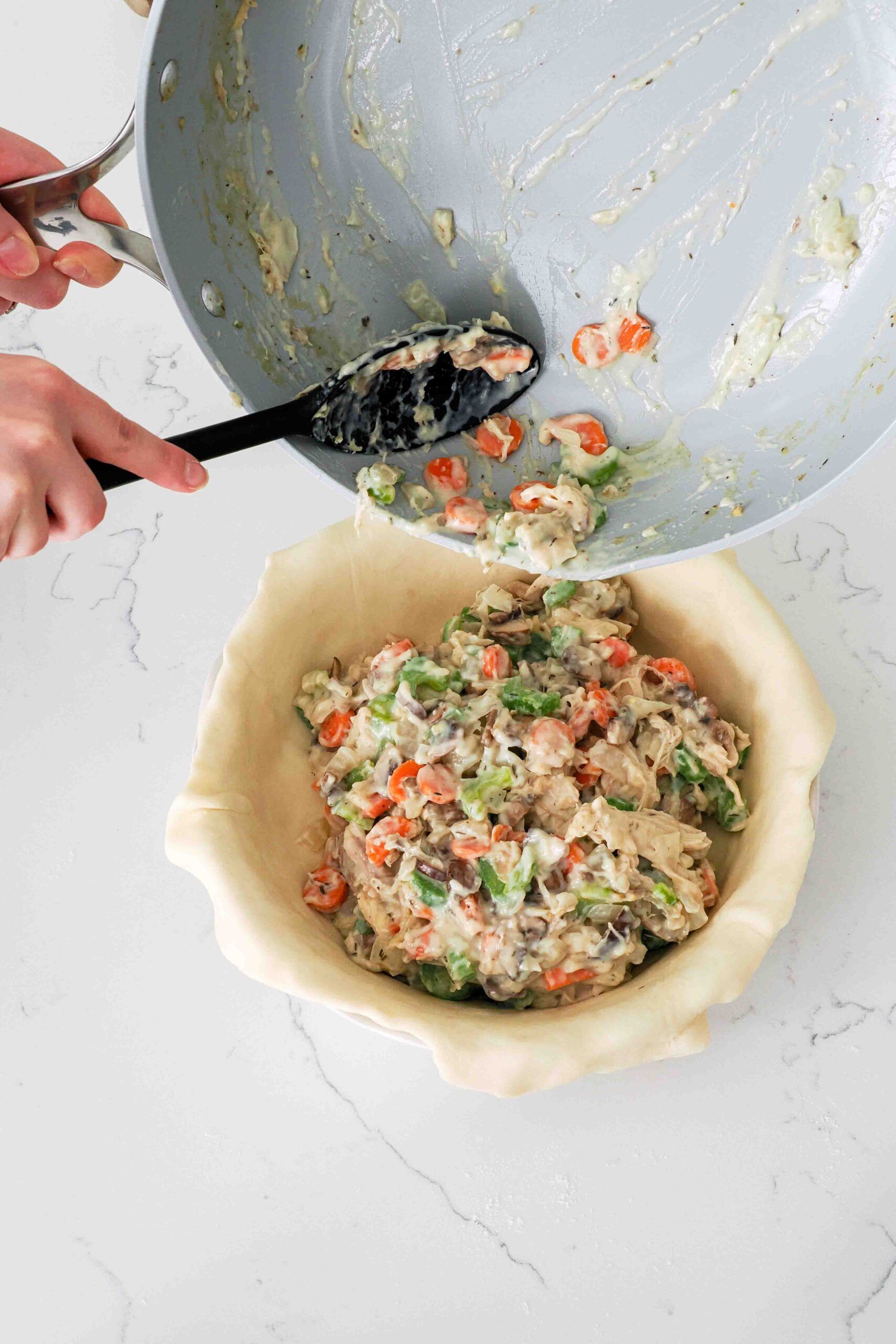 A spoon guides chicken pot pie filling into a pie dish lined with pie dough.
