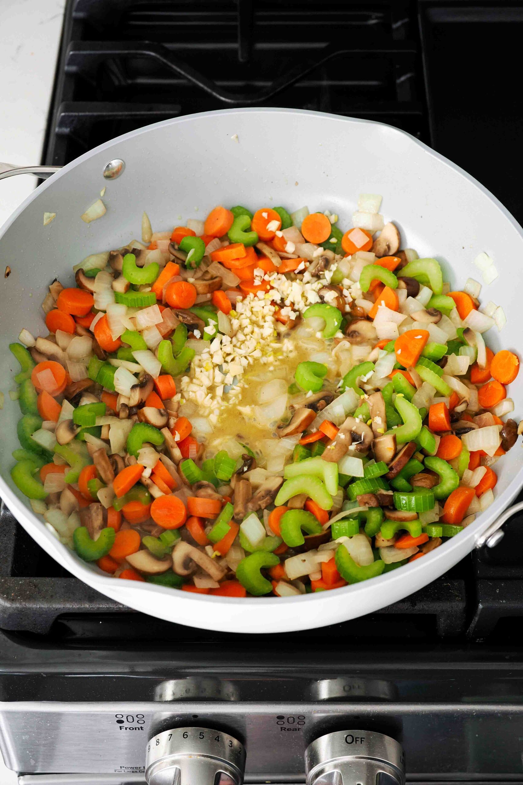 Garlic added to a large pan with onions, carrots, celery, and mushrooms.